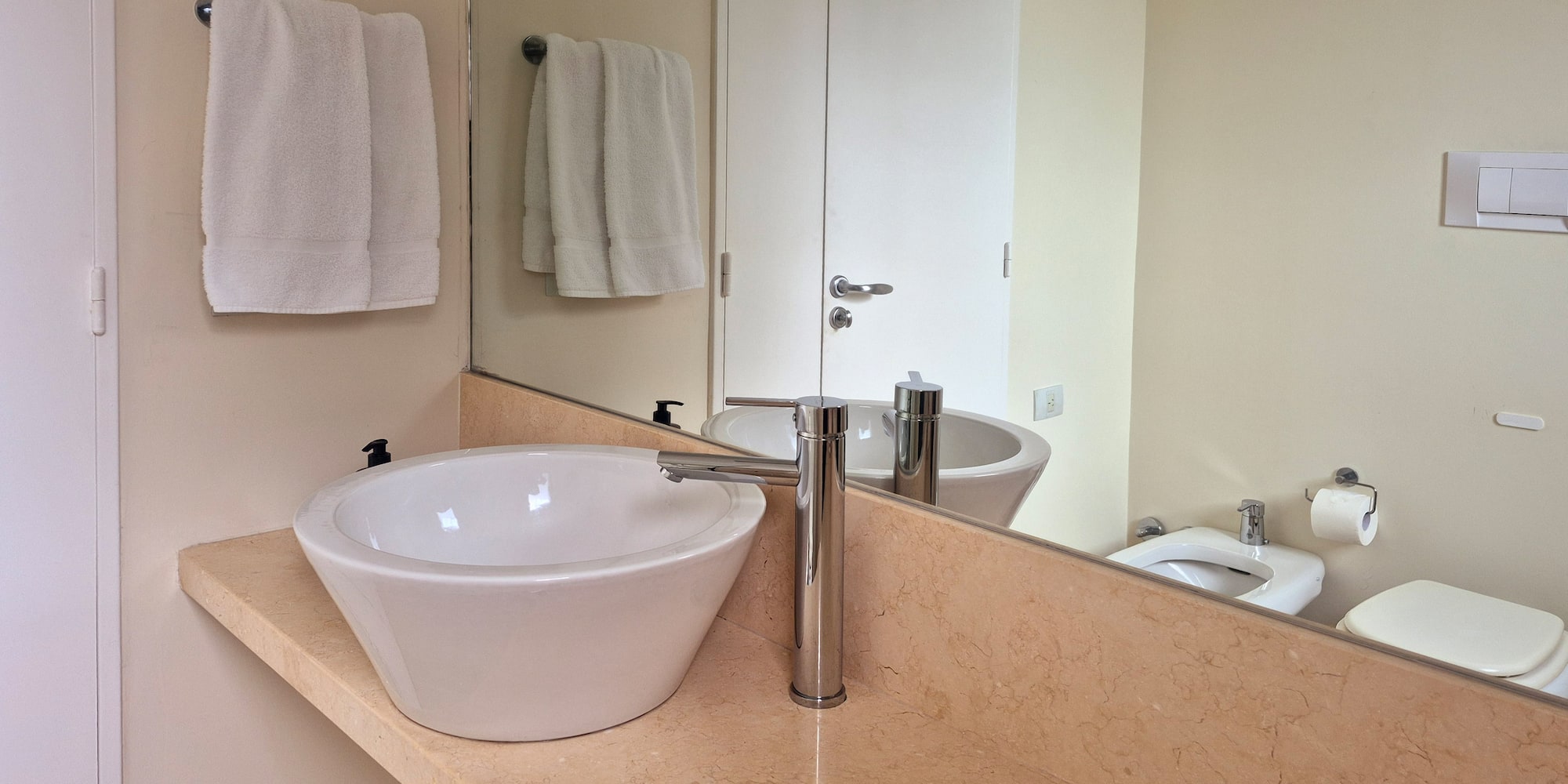 Modern bathroom with white vessel sink, chrome faucet, marble vanity, and mirror.