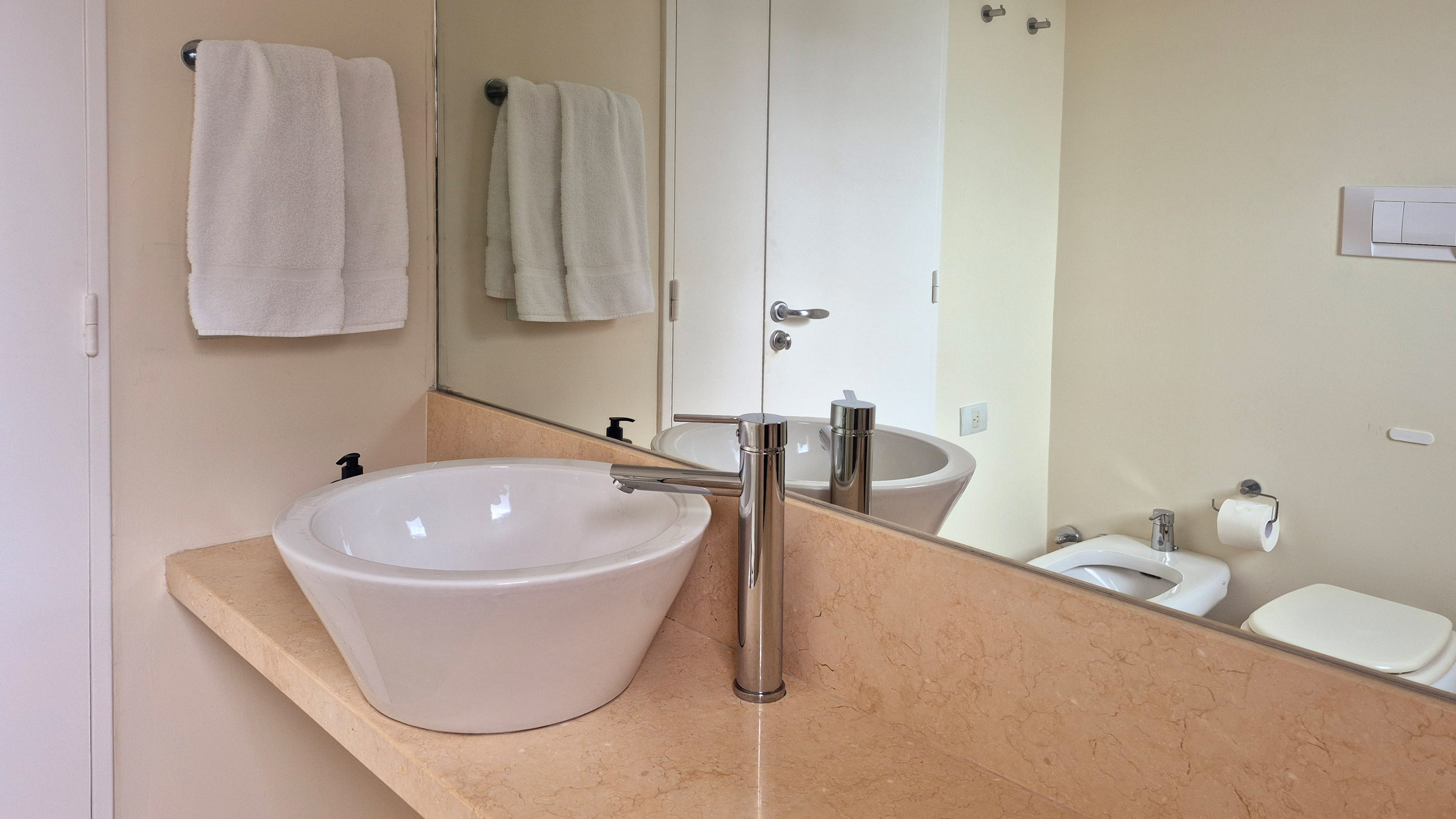Modern bathroom with white vessel sink, chrome faucet, marble vanity, and mirror.