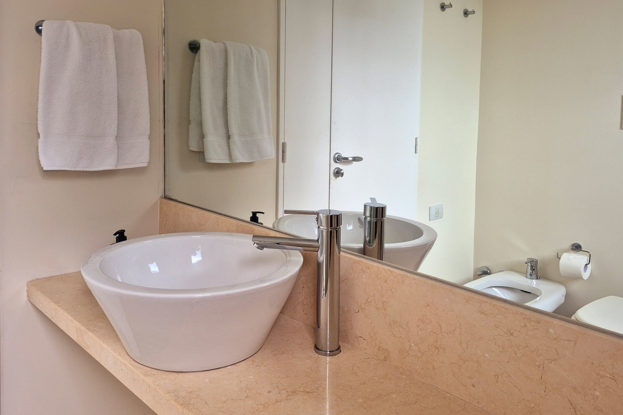 Modern bathroom with white vessel sink, chrome faucet, marble vanity, and mirror.