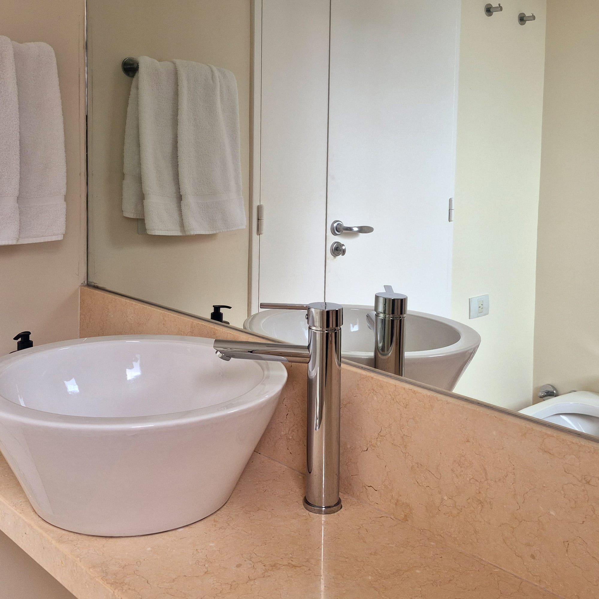 Modern bathroom with white vessel sink, chrome faucet, marble vanity, and mirror.