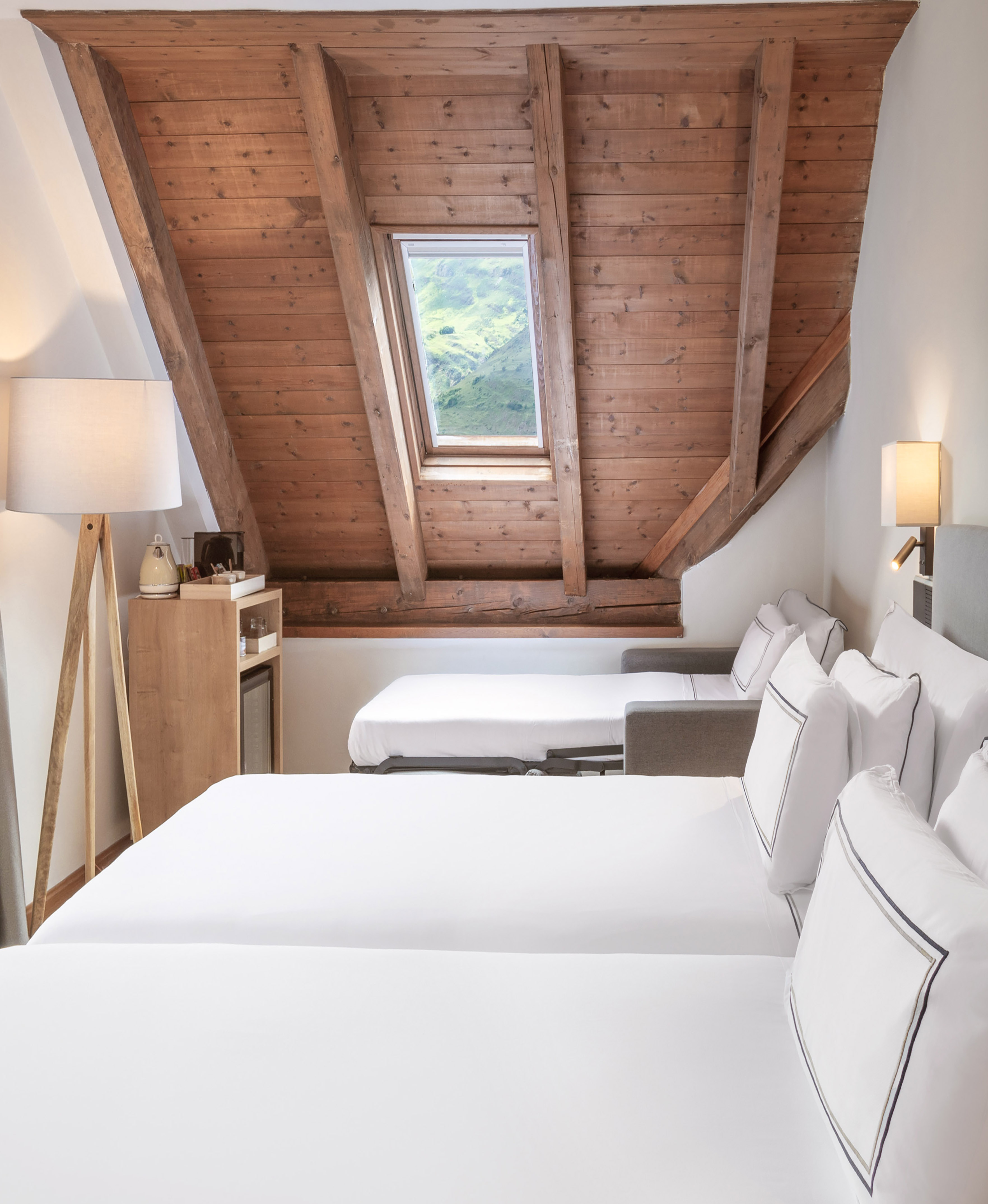 Hotel attic room with wooden ceiling, mountain view skylight, three beds.