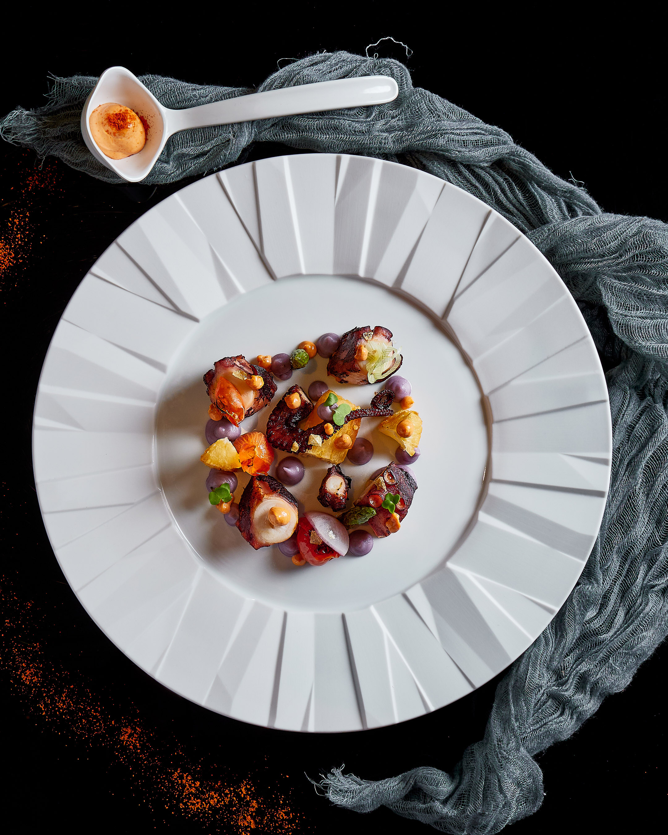 Gourmet grilled octopus, purple potato puree, orange sauce on white plate.