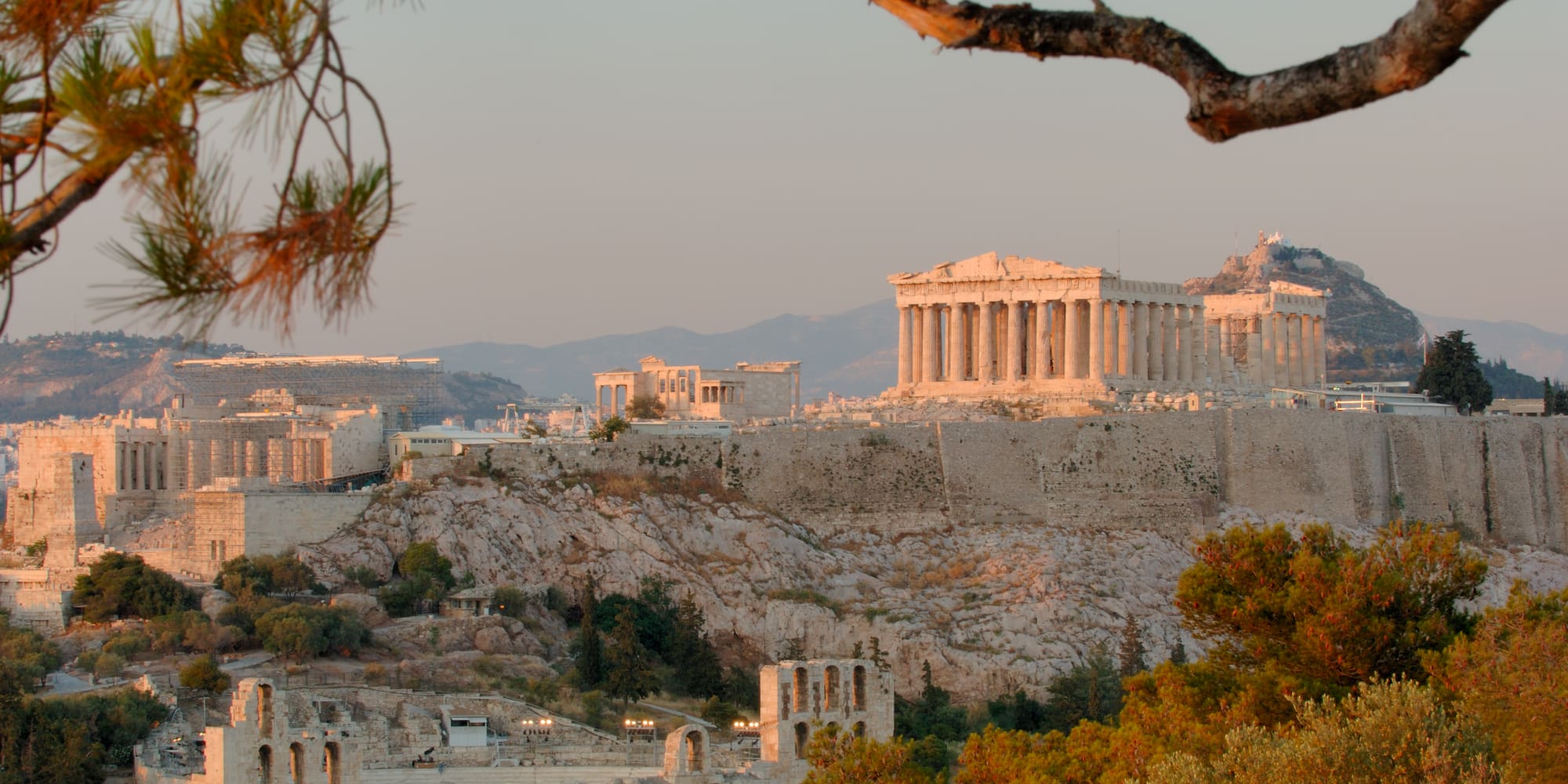 a stone buildings with columns and a hill with trees