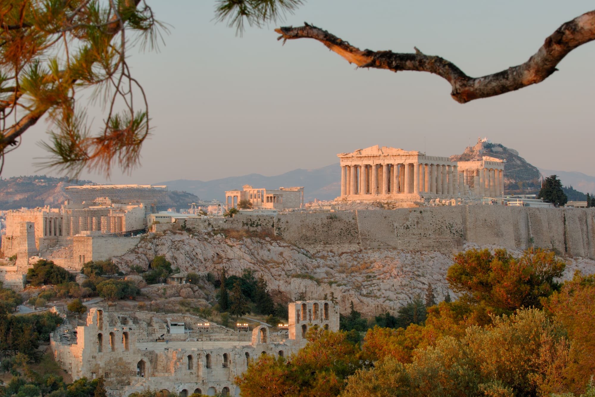 a stone buildings with columns and a hill with trees
