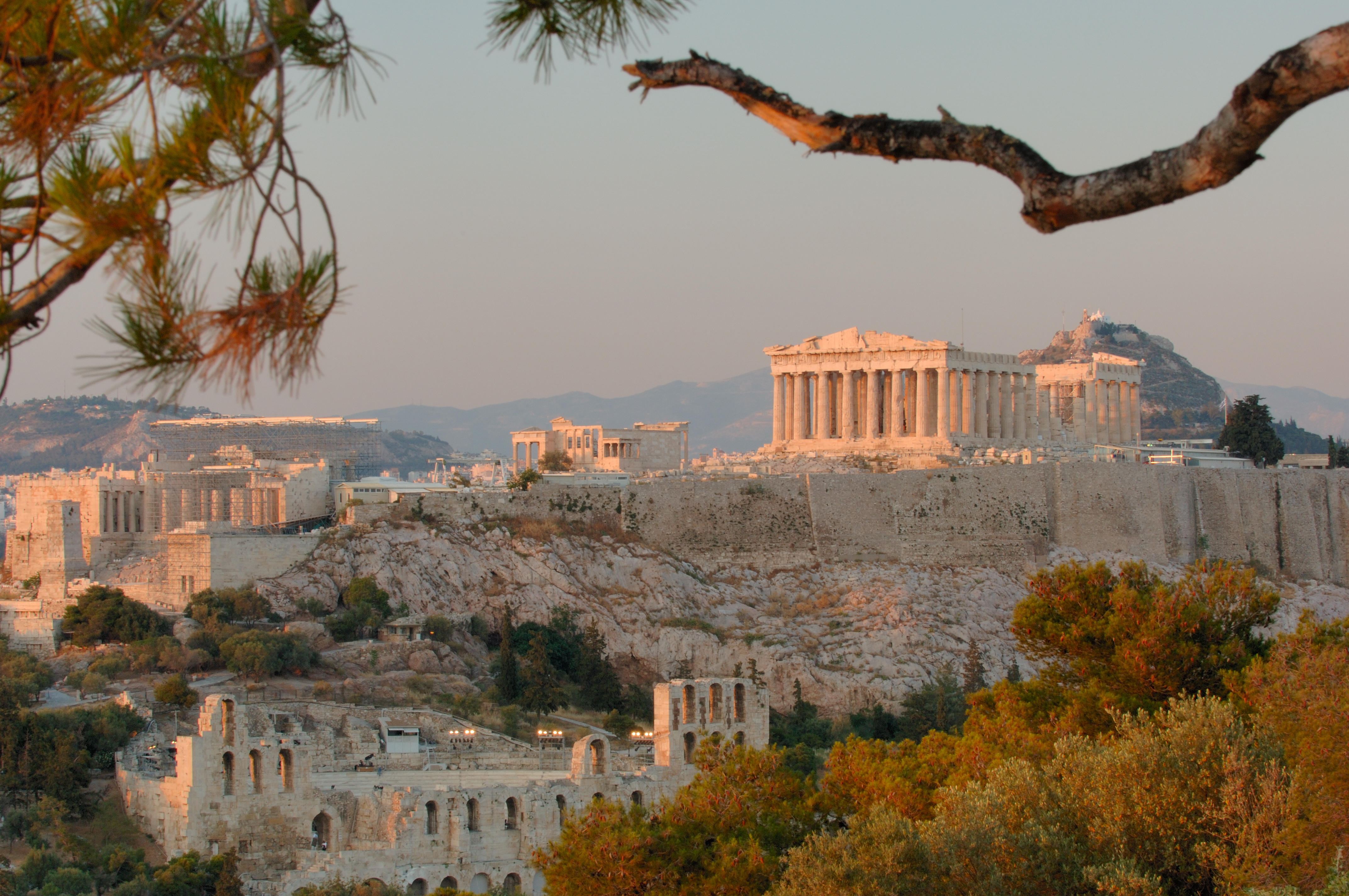 a stone buildings with columns and a hill with trees