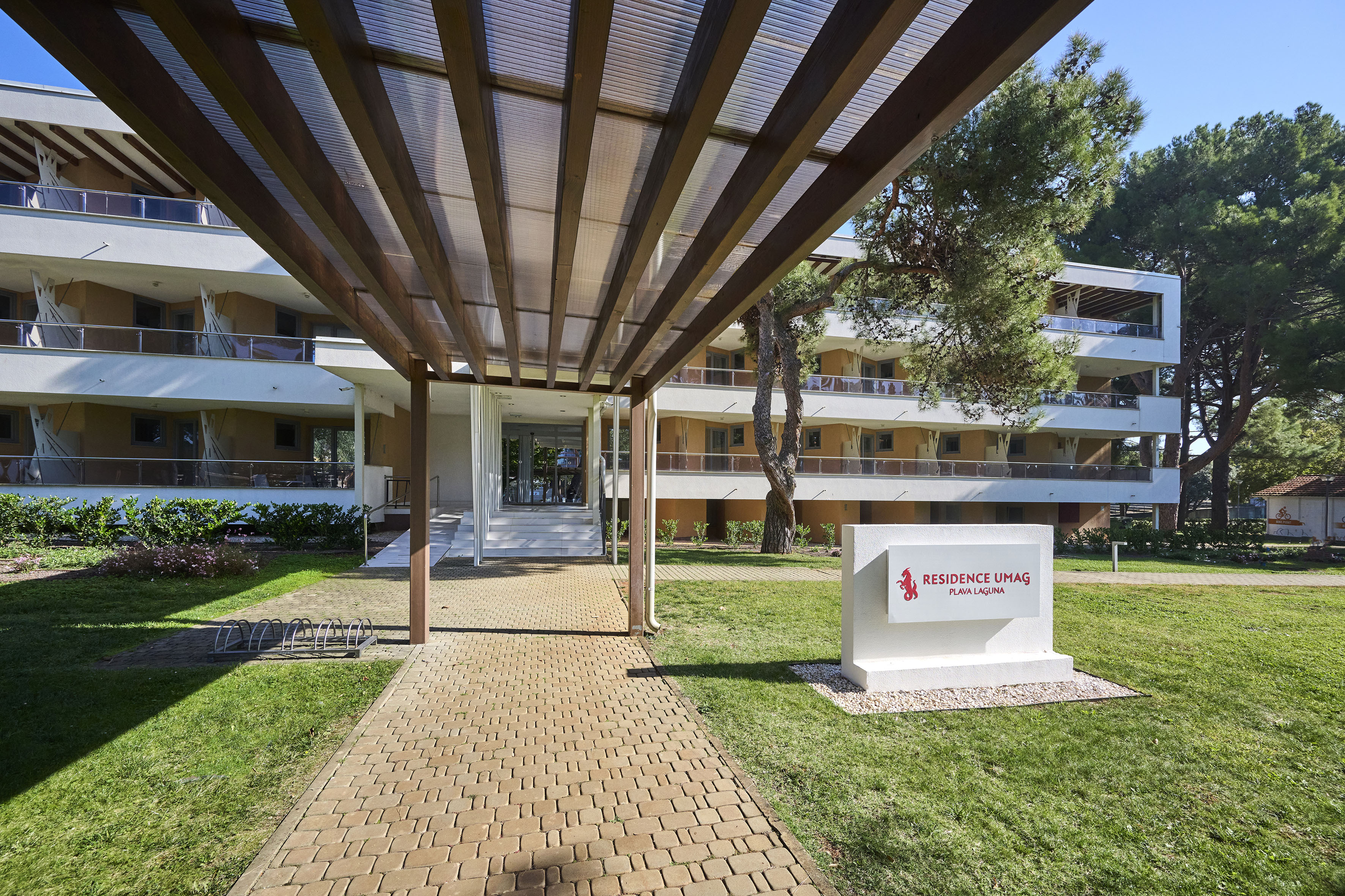 a walkway with a sign and grass in front of a building