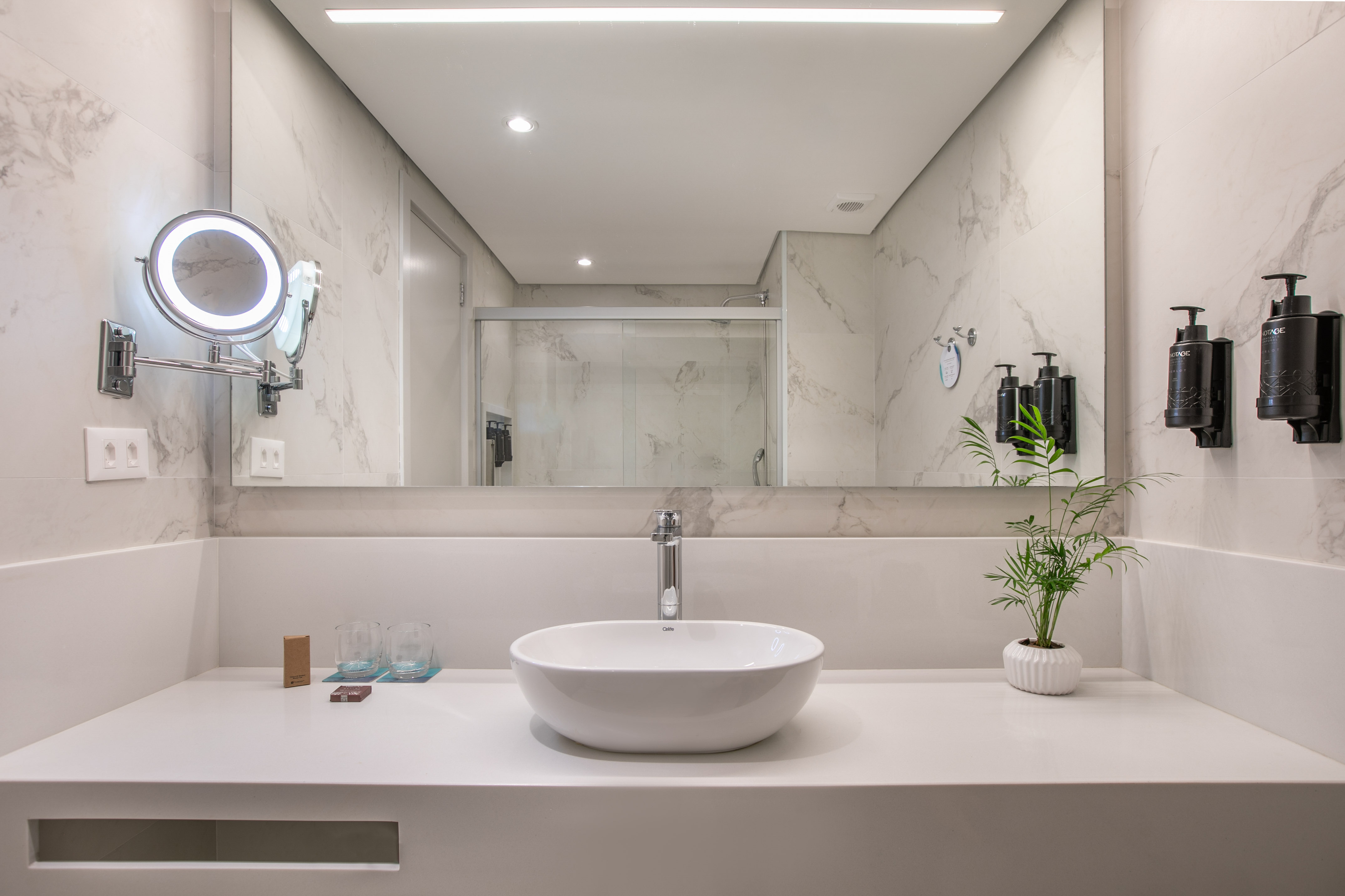 Modern hotel bathroom vanity, white vessel sink, marble walls, lighted mirror.