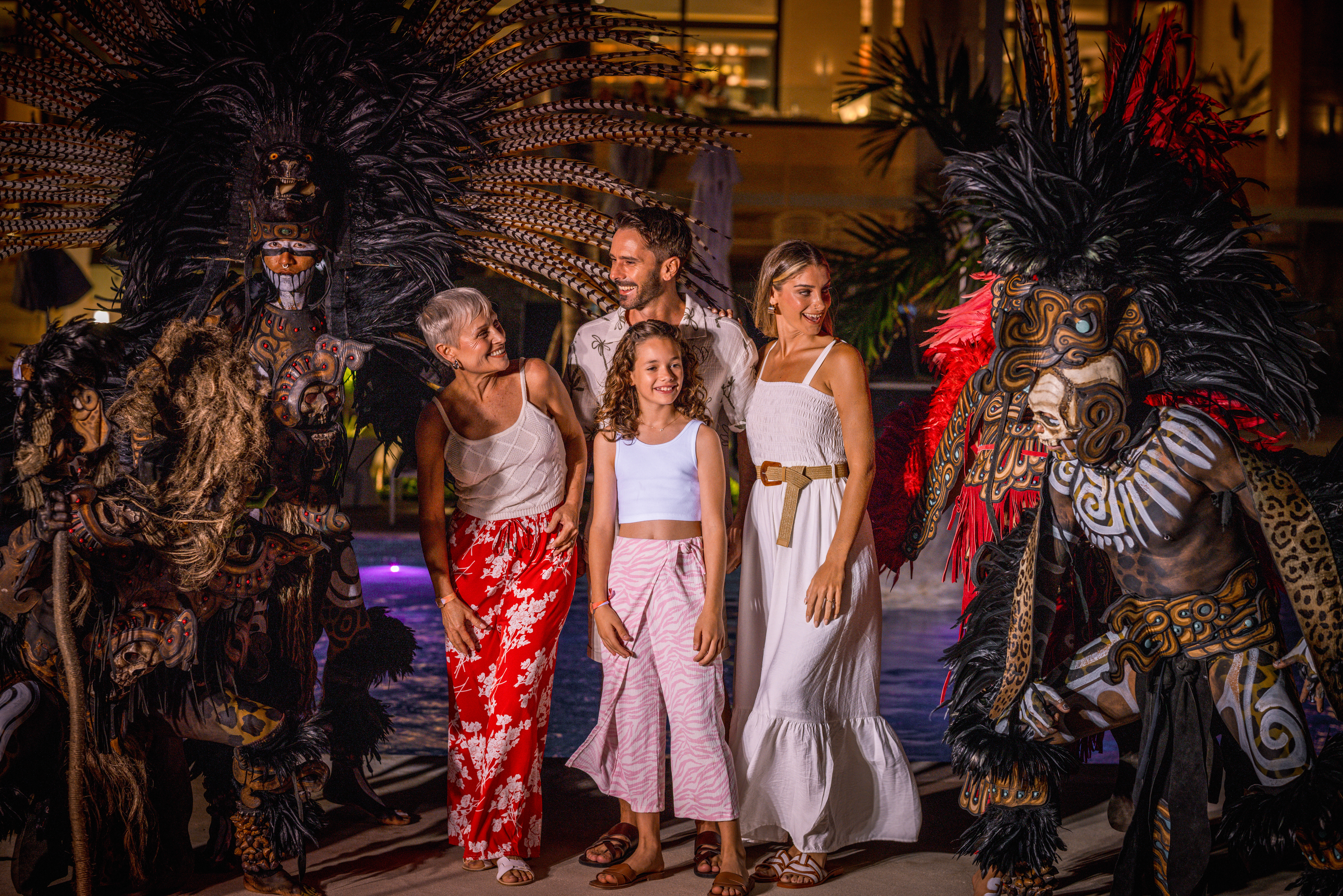 Family with performers in ornate feathered tribal costumes at a resort.