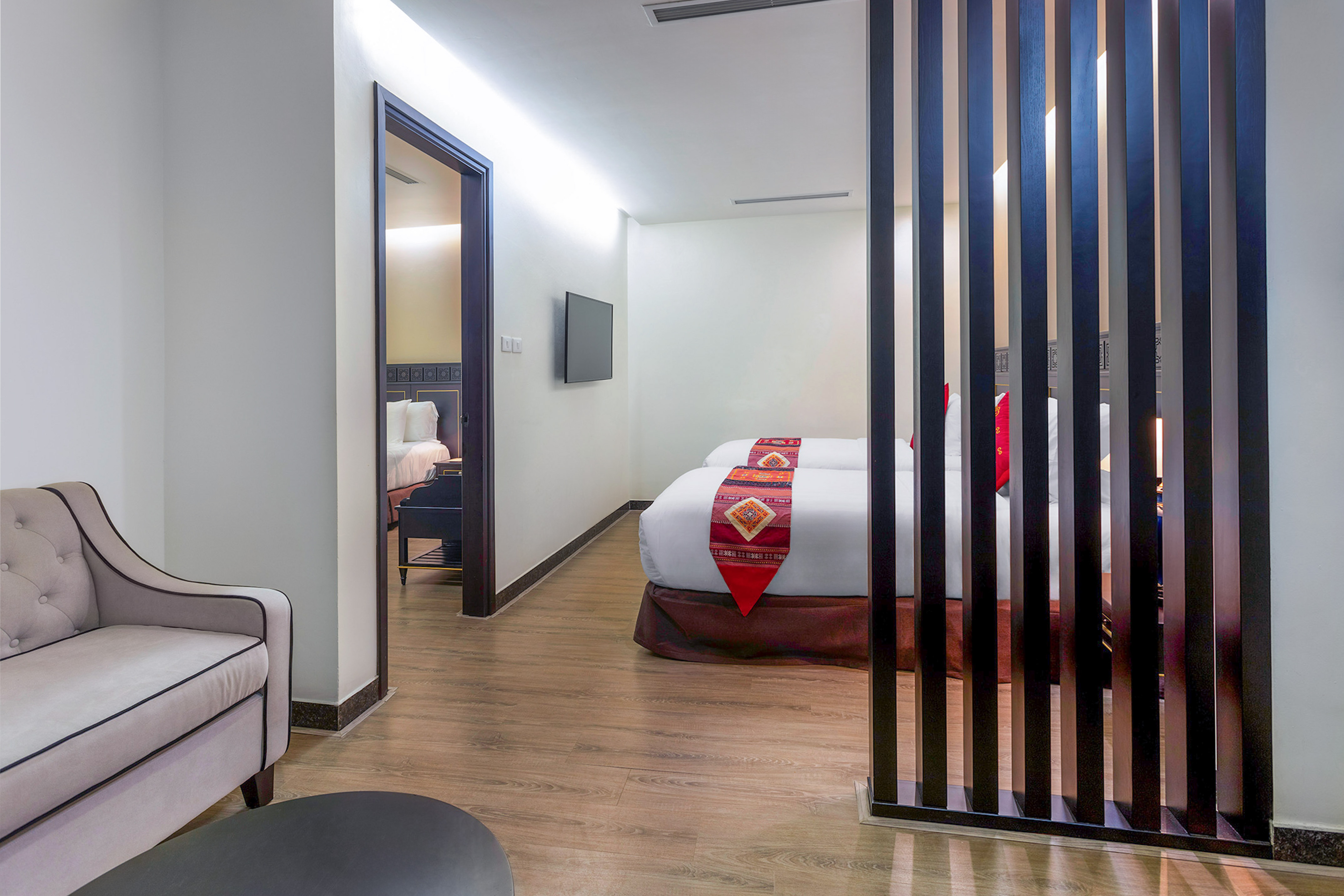 Modern hotel suite with twin beds, armchair, and stylish wooden partition.
