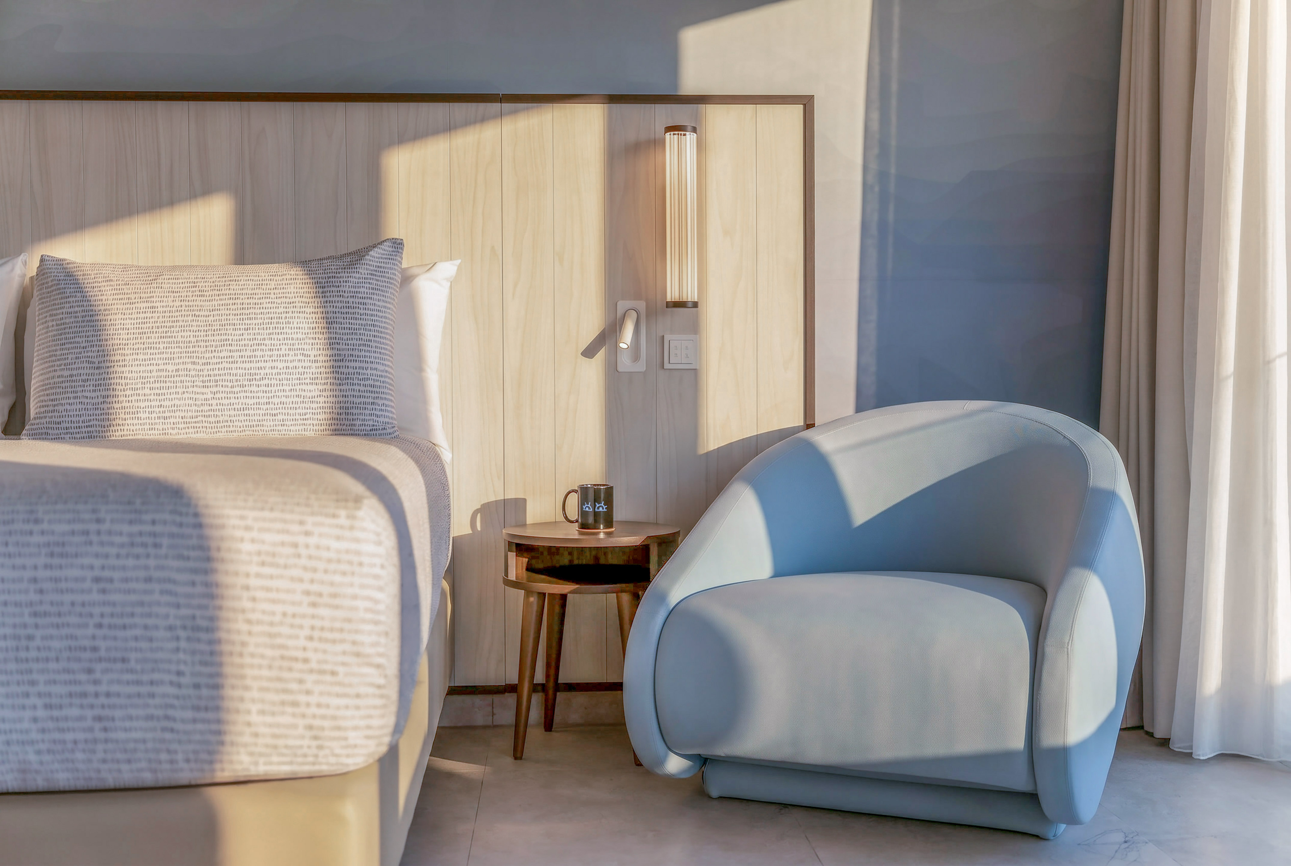 Modern bedroom with wood headboard, blue accent chair, and side table.