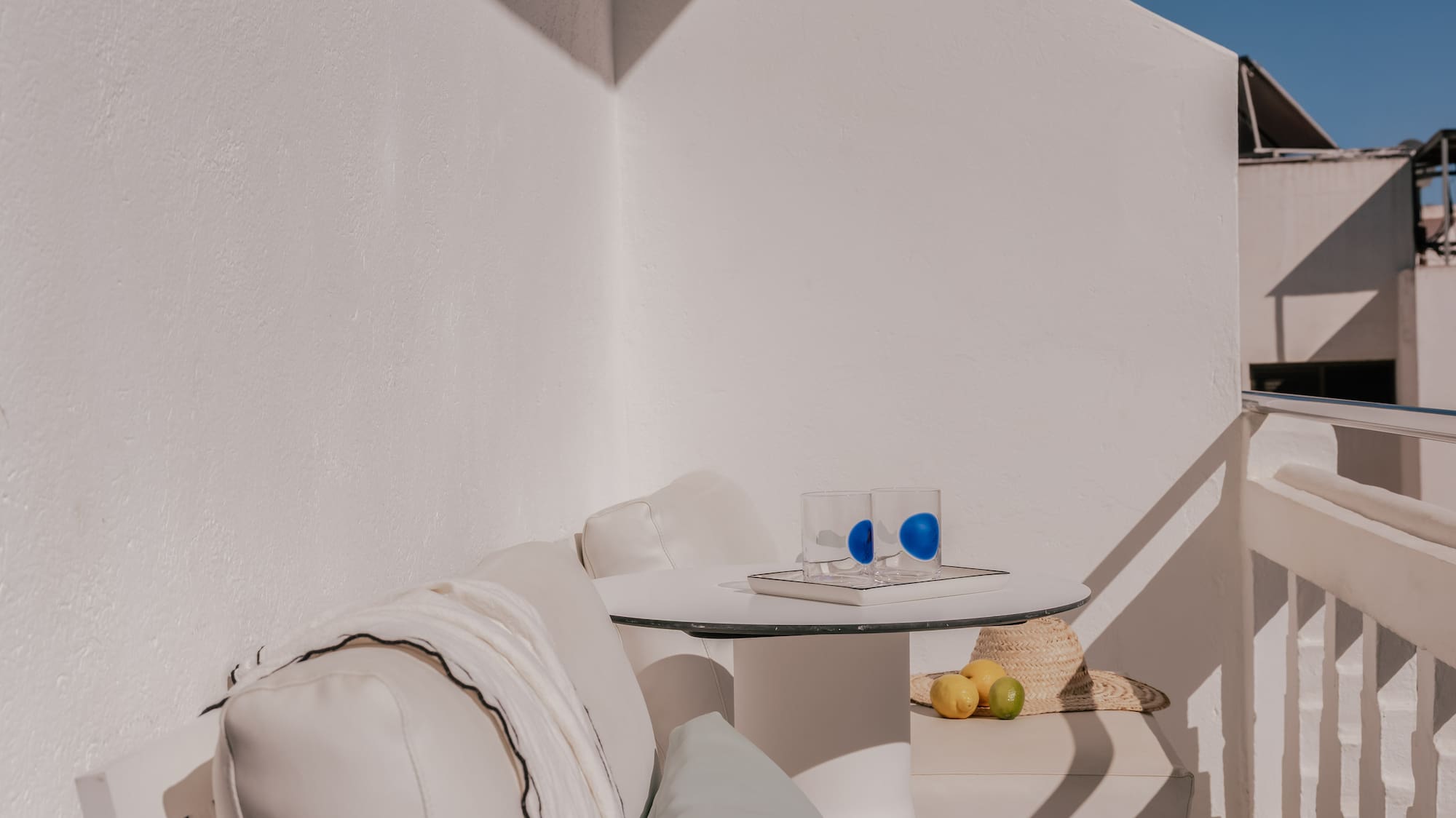 Modern white balcony with sofa, table, straw hat, and blue sky.