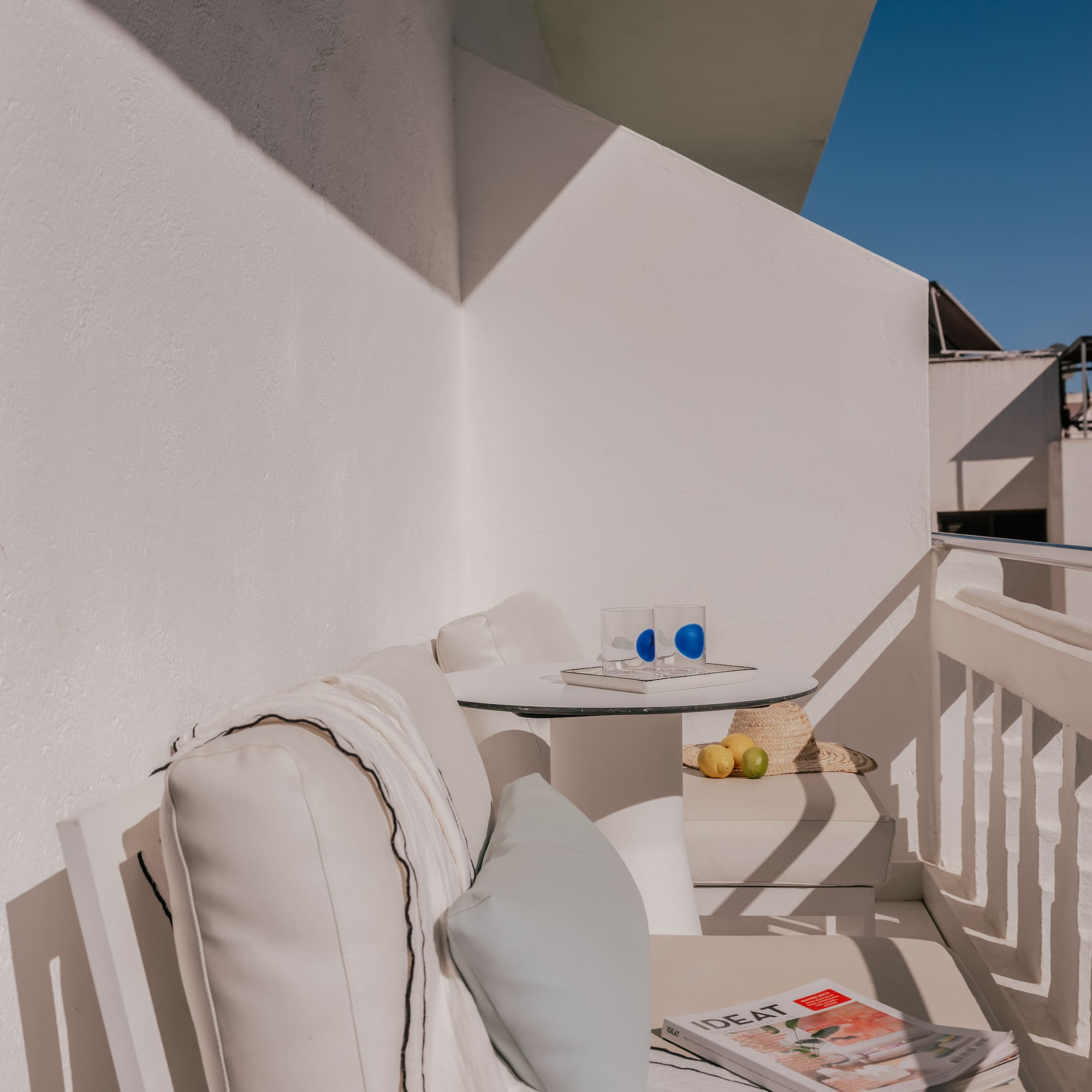 Minimalist white outdoor balcony with lounge sofa, table, and blue sky.