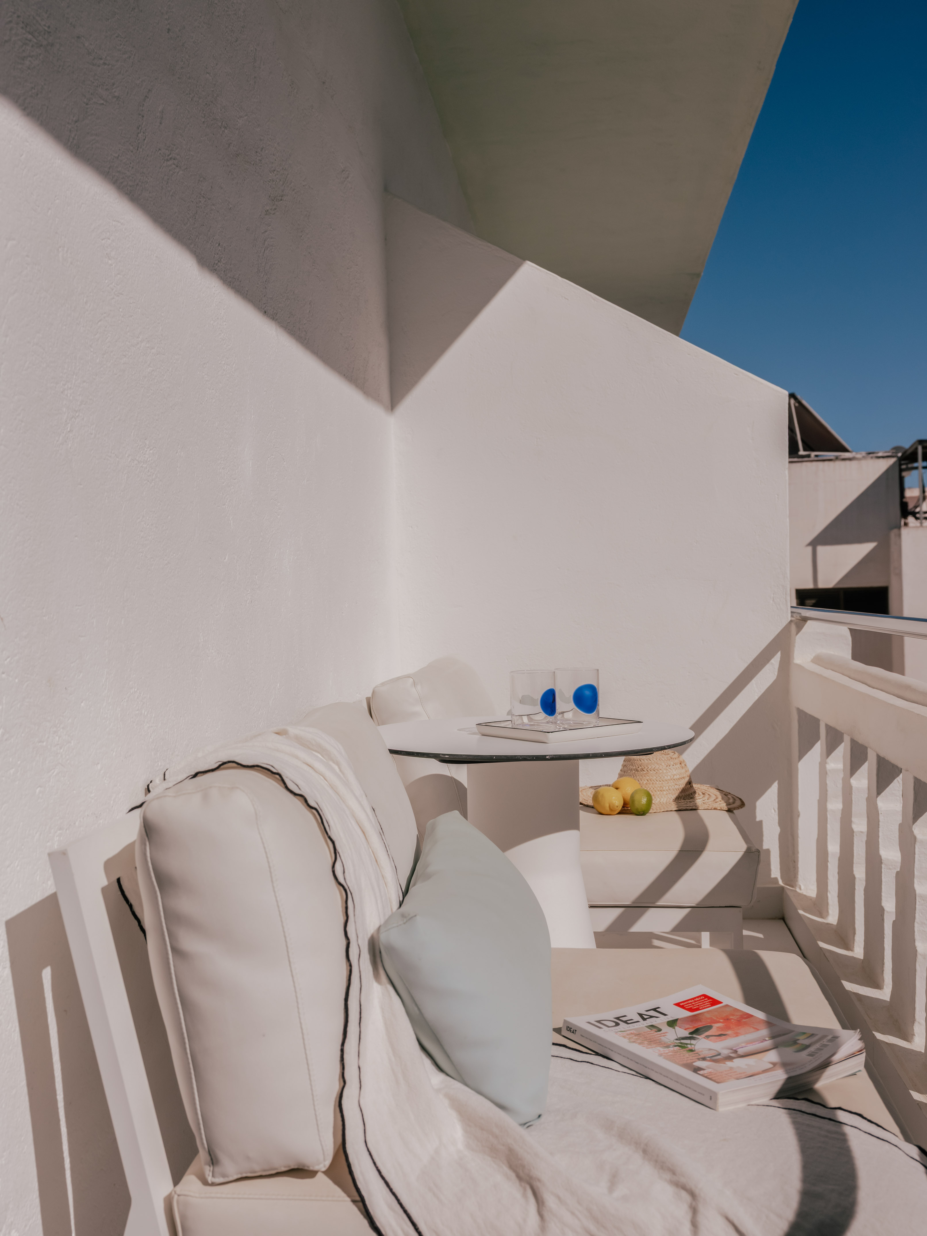 Minimalist white outdoor balcony with lounge sofa, table, and blue sky.