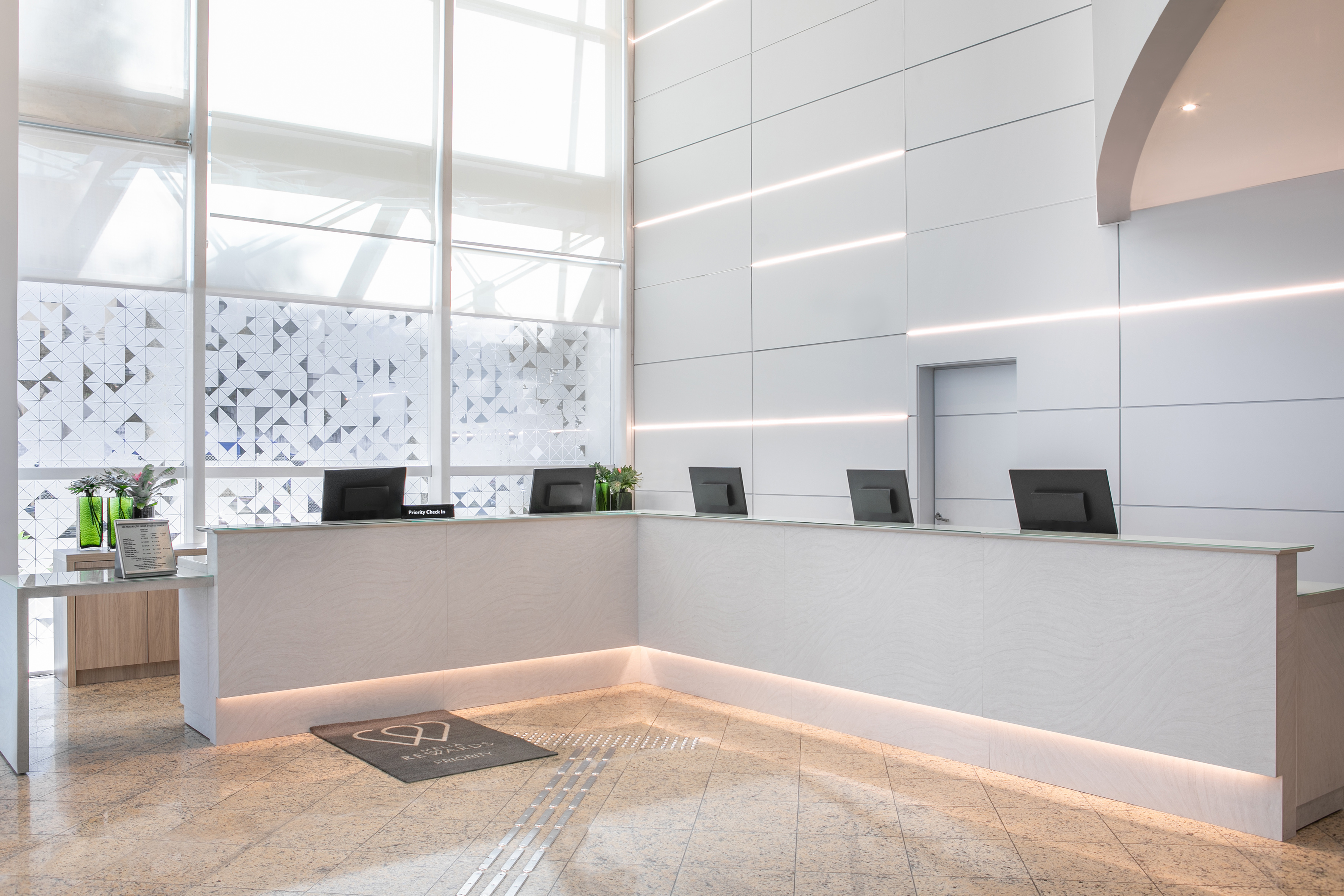 Modern hotel lobby reception desk with white walls and patterned windows.