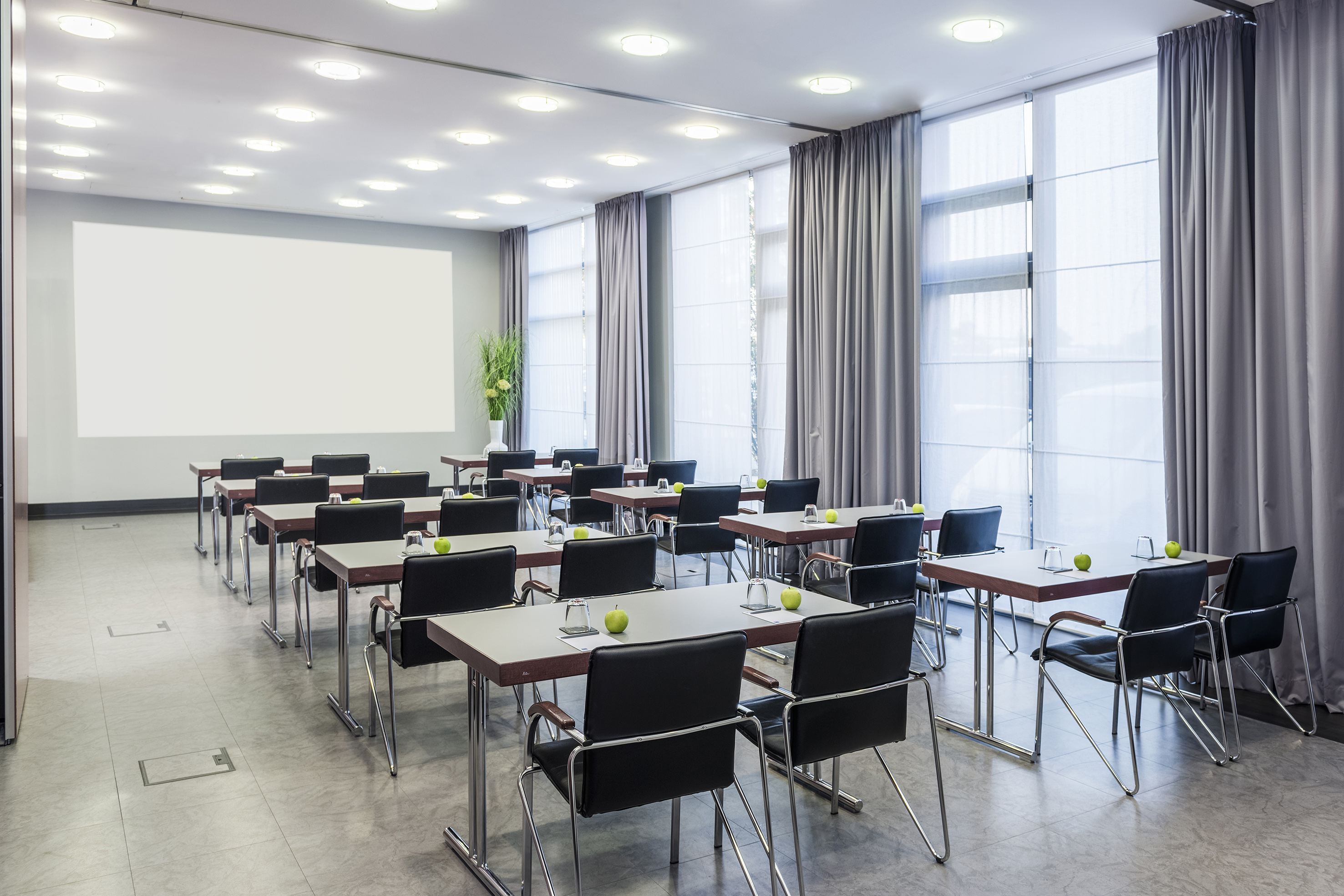 Modern conference room with projection screen, tables, black chairs, and apples.