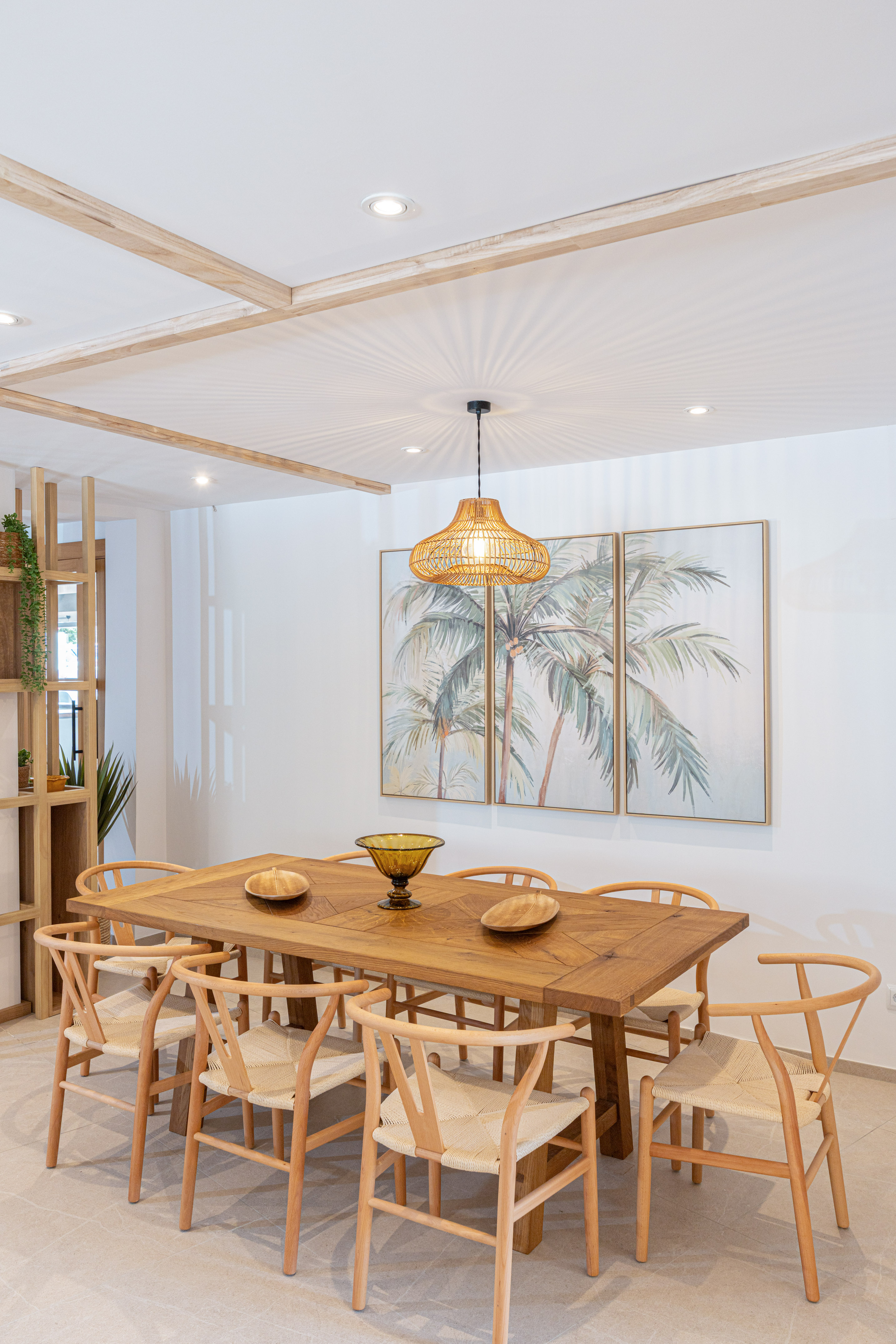 Tropical dining room: wooden table, chairs, woven light, and palm tree art.