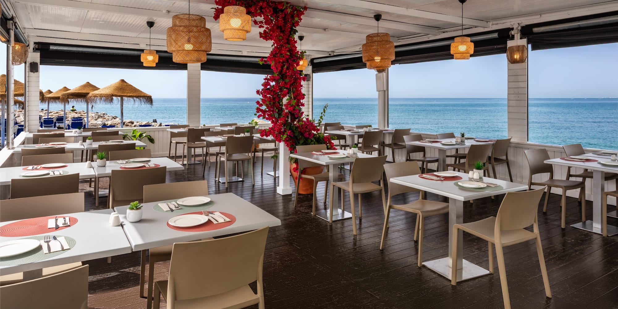Beachfront restaurant with sea views, set tables, and red floral decor.