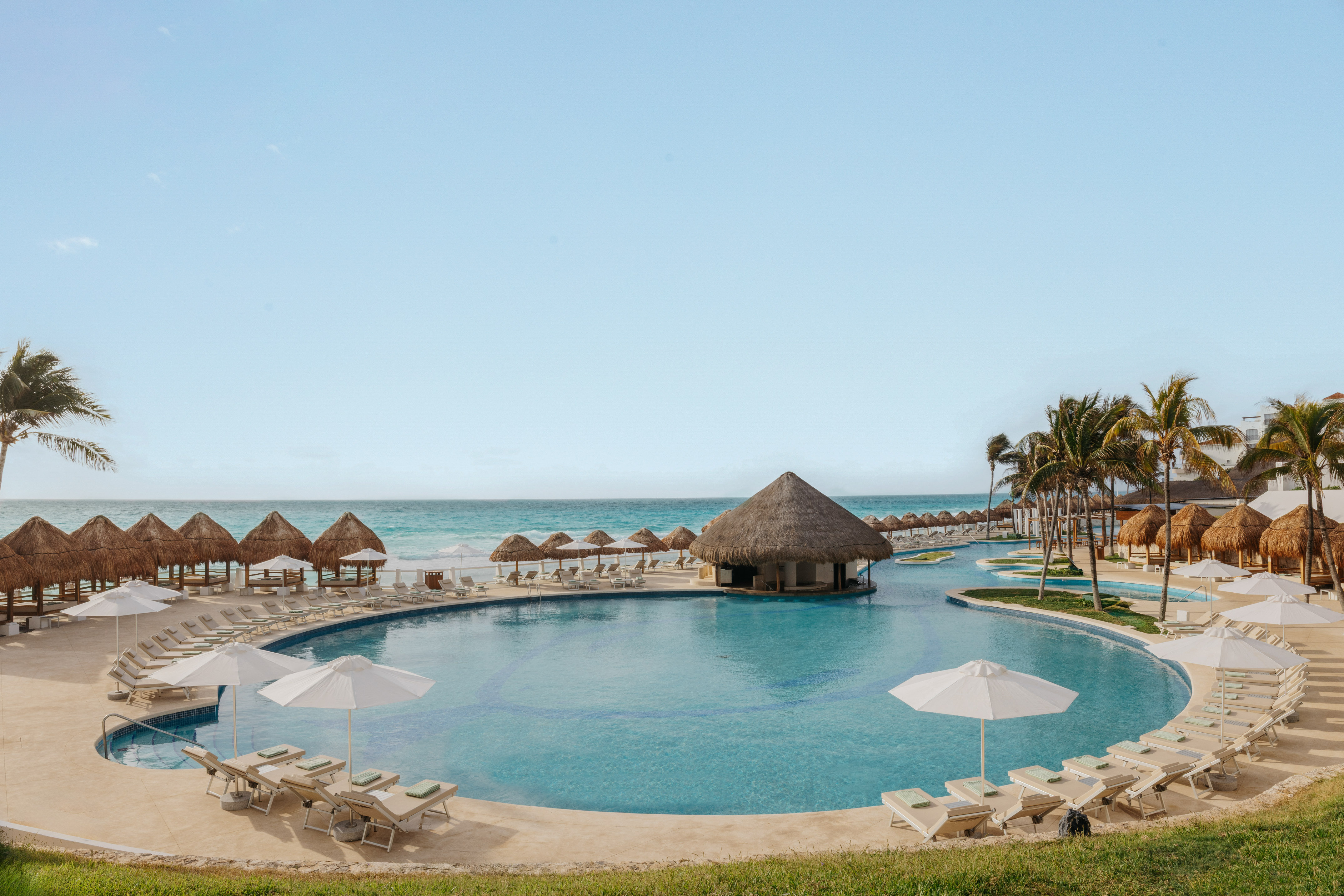Resort pool with swim-up bar, beach, palapas, and palm trees.
