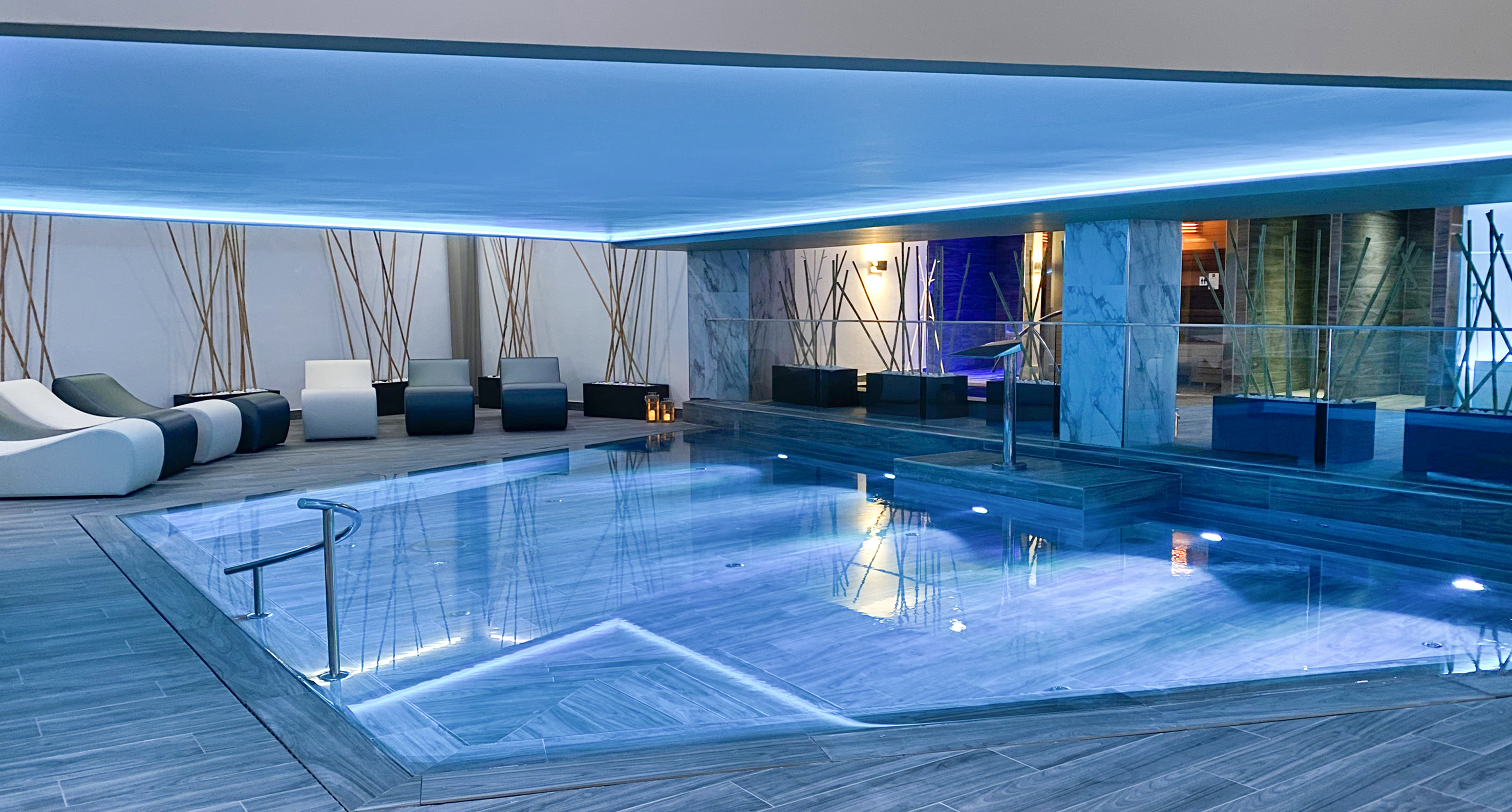 Blue-lit indoor spa pool with loungers in a modern wellness center.