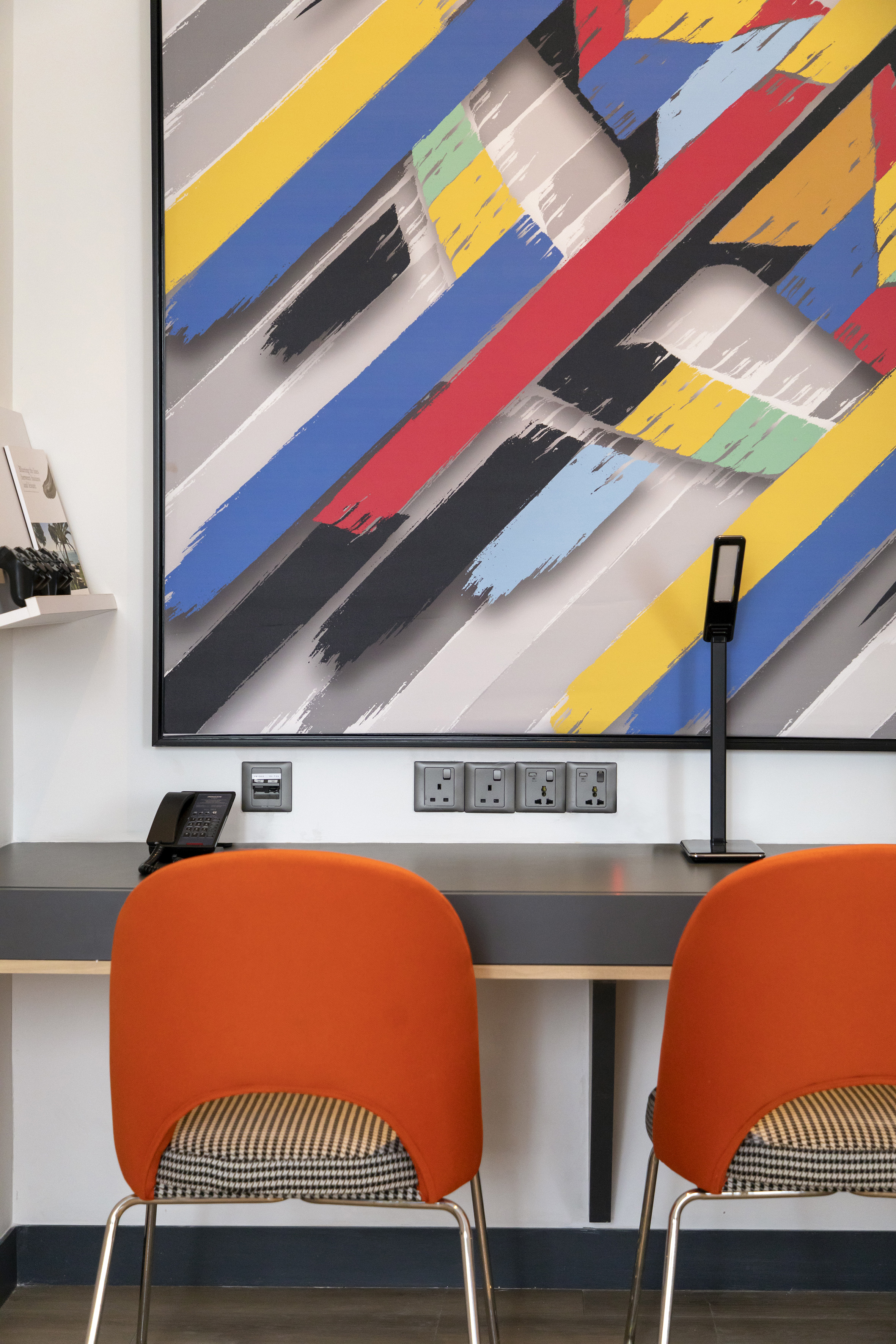 Modern desk with vibrant abstract art, orange chairs, and power outlets.