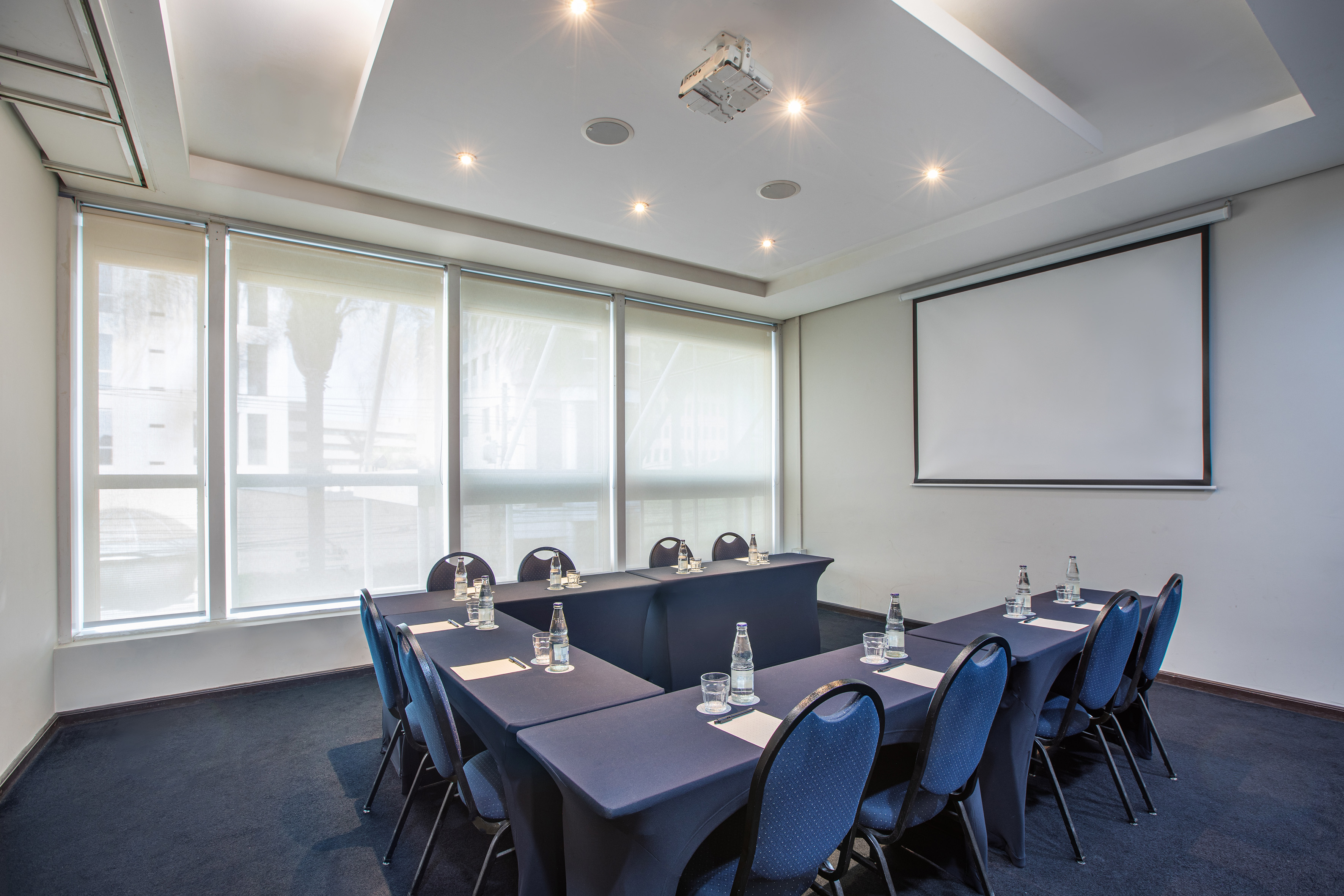 Modern conference room with U-shaped table, blue chairs, and projector screen.
