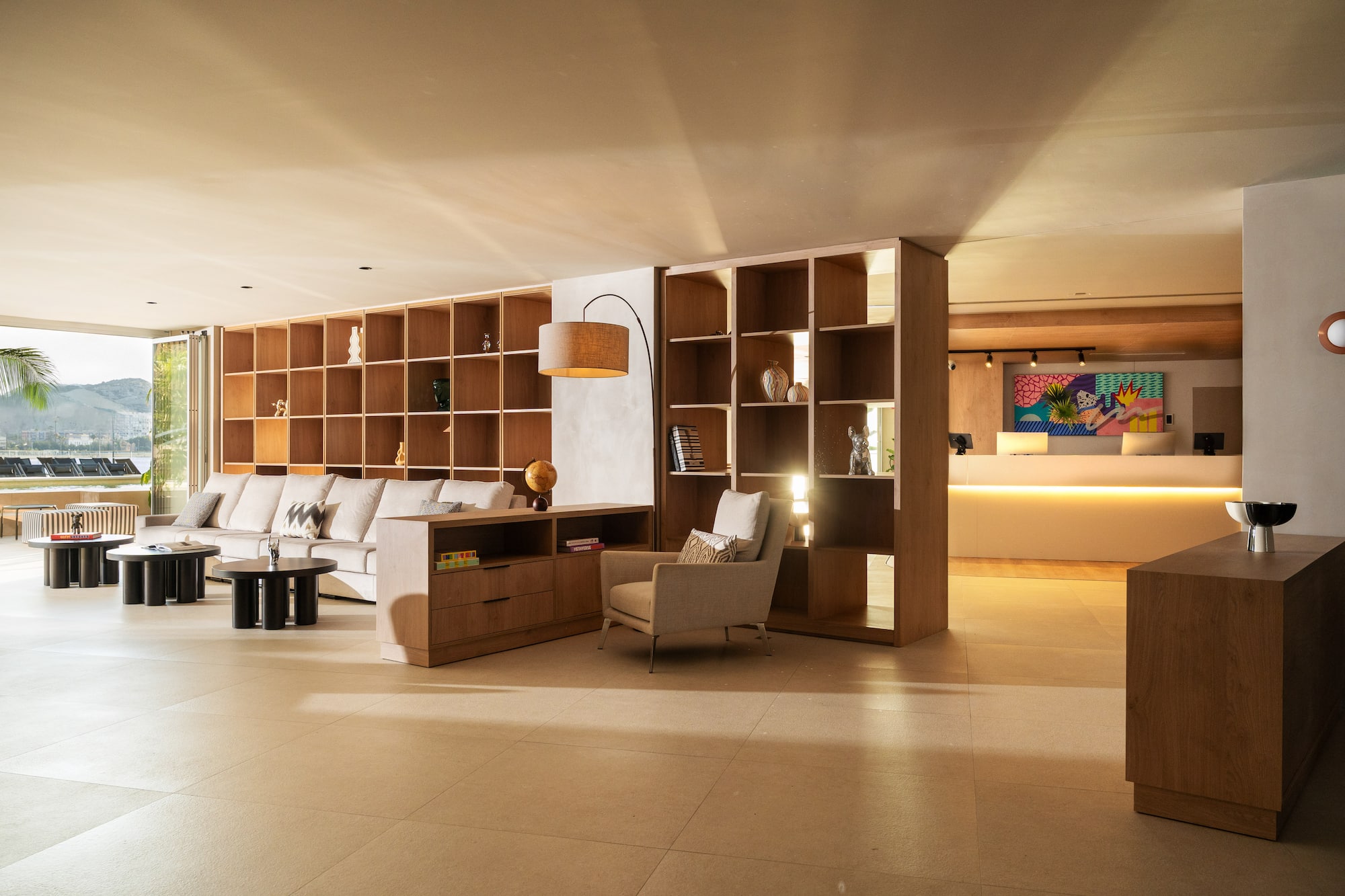 Modern hotel lounge with wooden shelves, sofa, armchairs, and reception area.