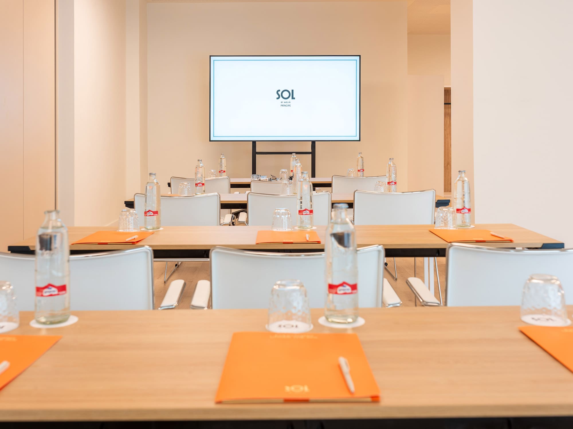 Bright conference room with Sol by Meliá logo on screen, tables, white chairs, water.