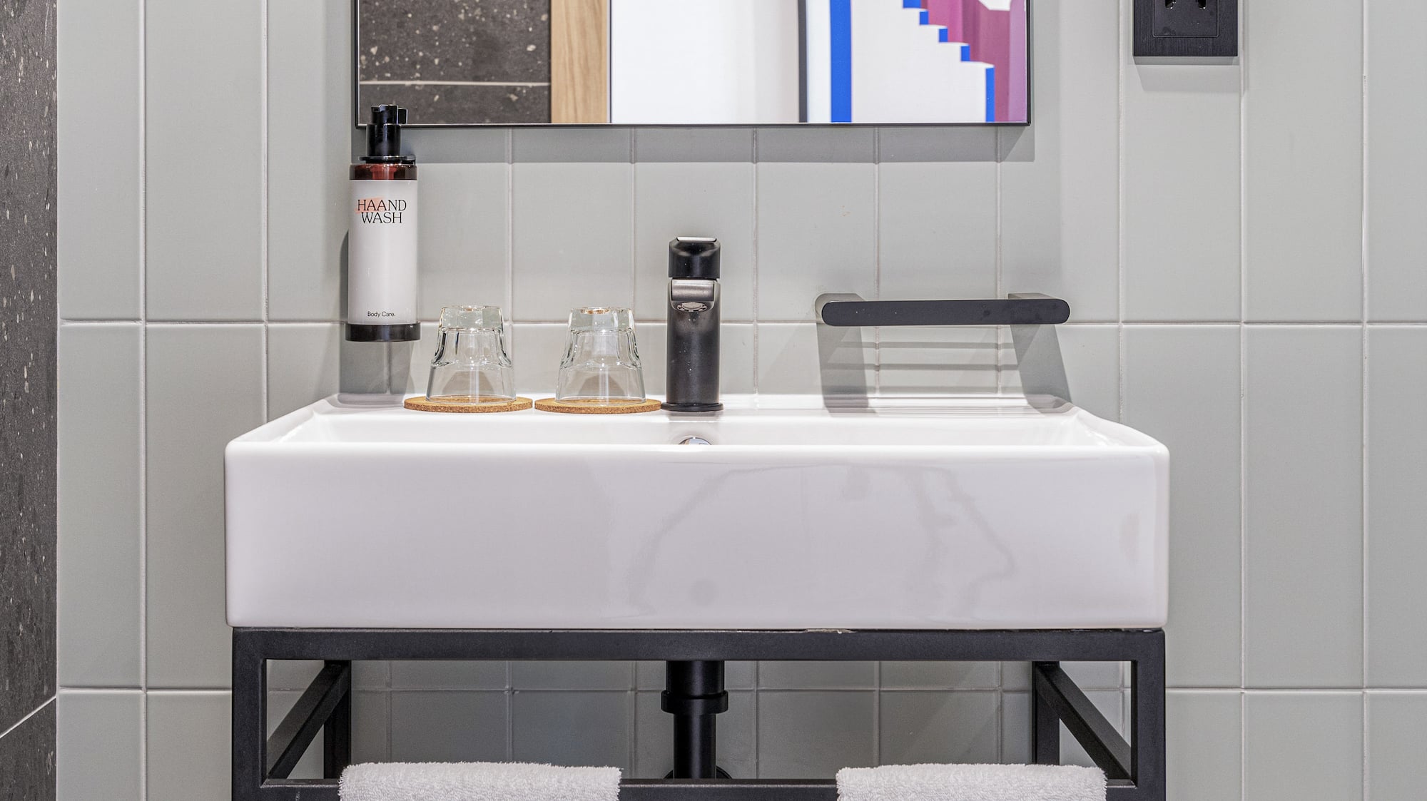 Modern bathroom vanity: white sink, black faucet, mirror, grey tiles, white towels.