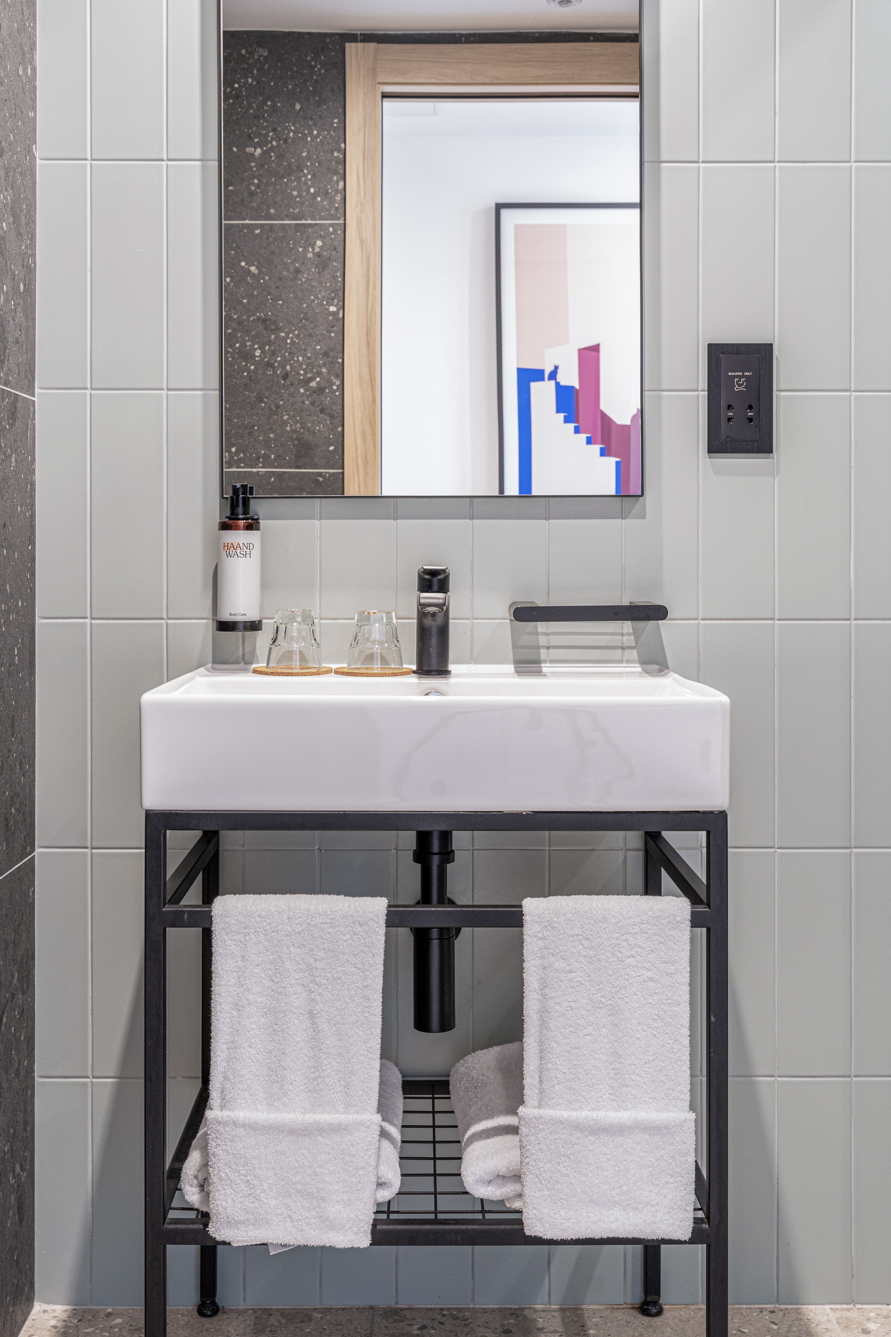 Modern bathroom vanity: white sink, black faucet, mirror, grey tiles, white towels.