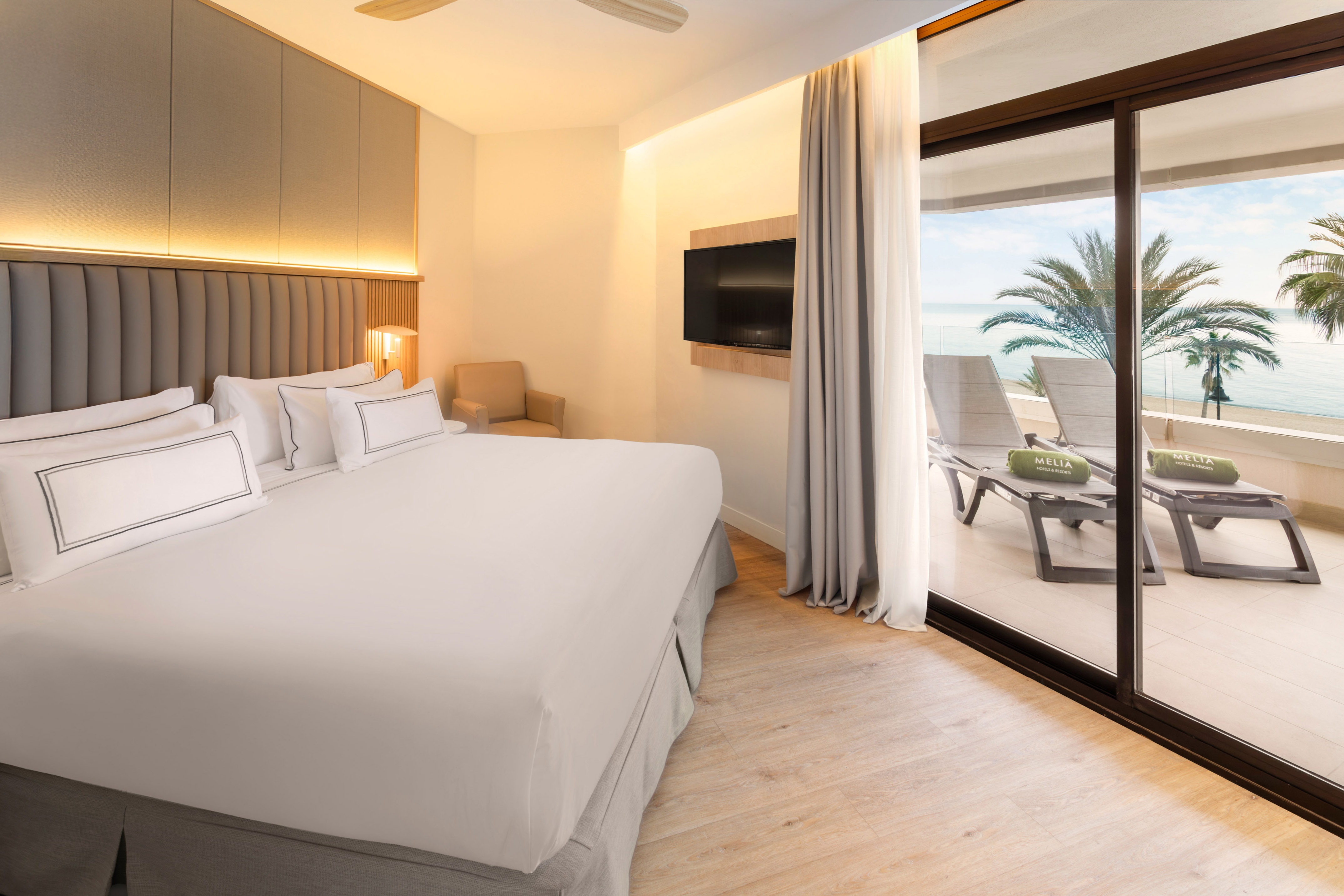 Resort hotel room with king bed, ocean view balcony, and loungers.