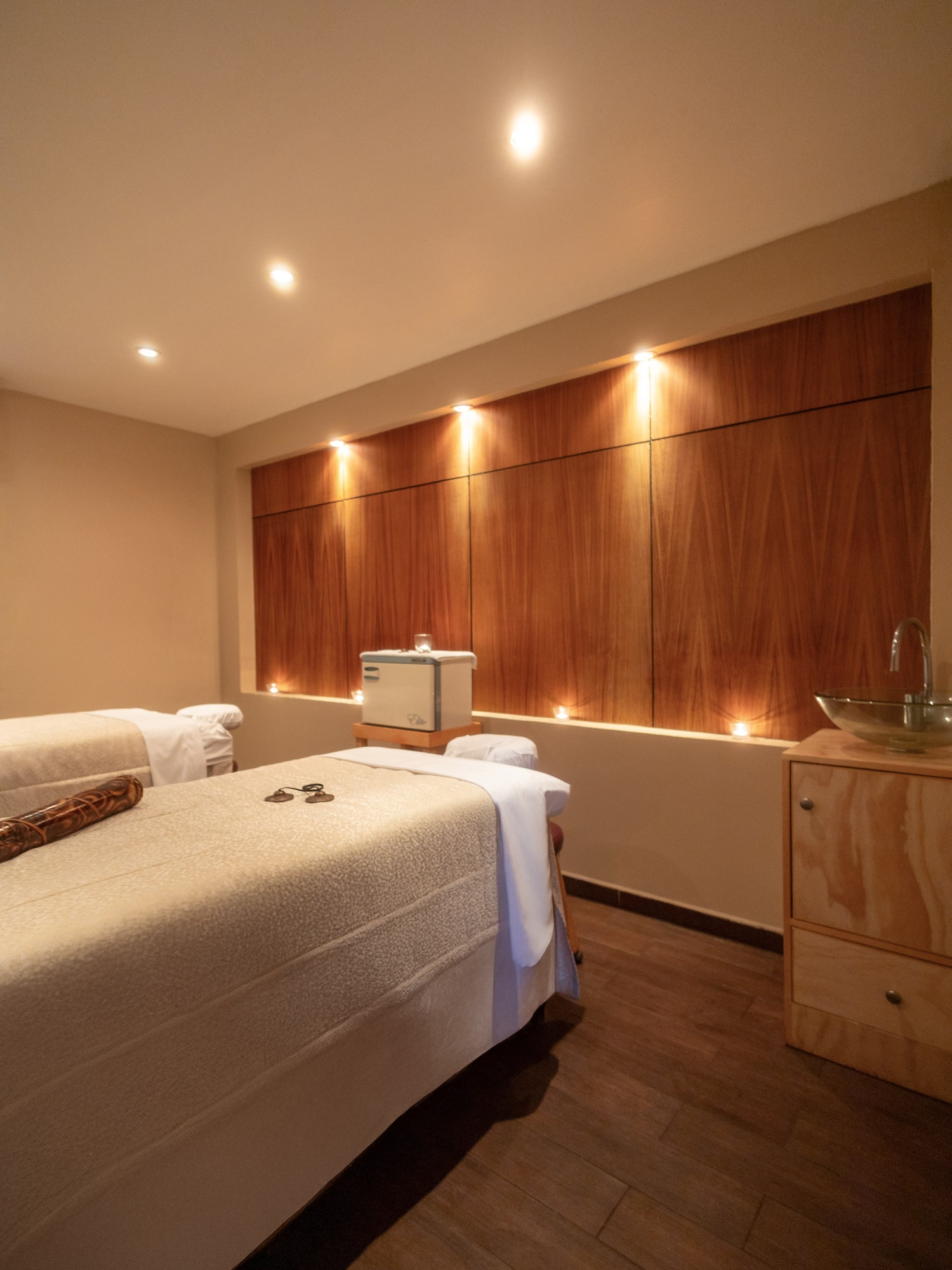 Inviting spa massage room with two tables, warm lighting, and wood accent wall.