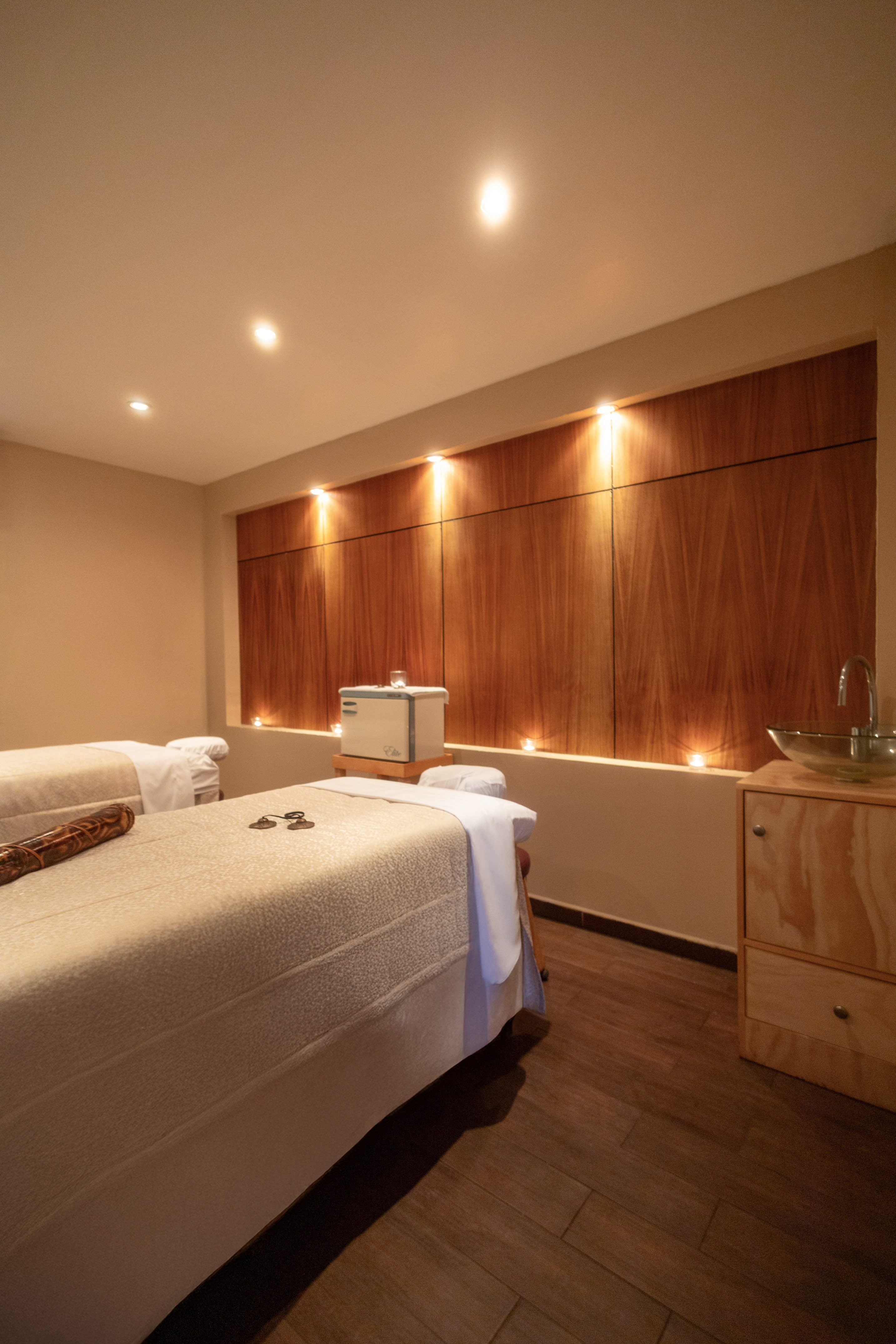 Inviting spa massage room with two tables, warm lighting, and wood accent wall.