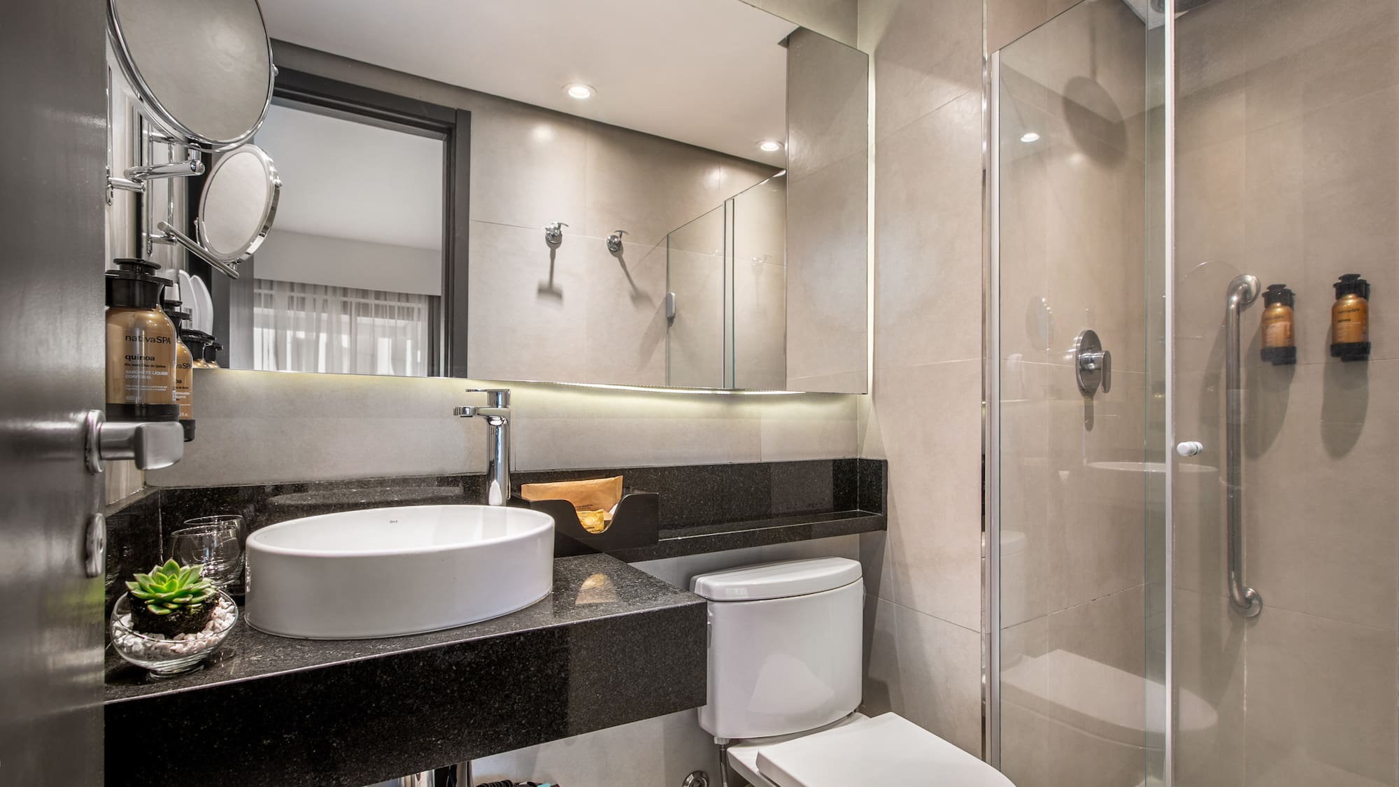 Modern hotel bathroom with white vessel sink, black granite vanity, toilet, and glass shower enclosure. - Deluxe Queen Room com Varanda - Meliá Ibirapuera, São Paulo