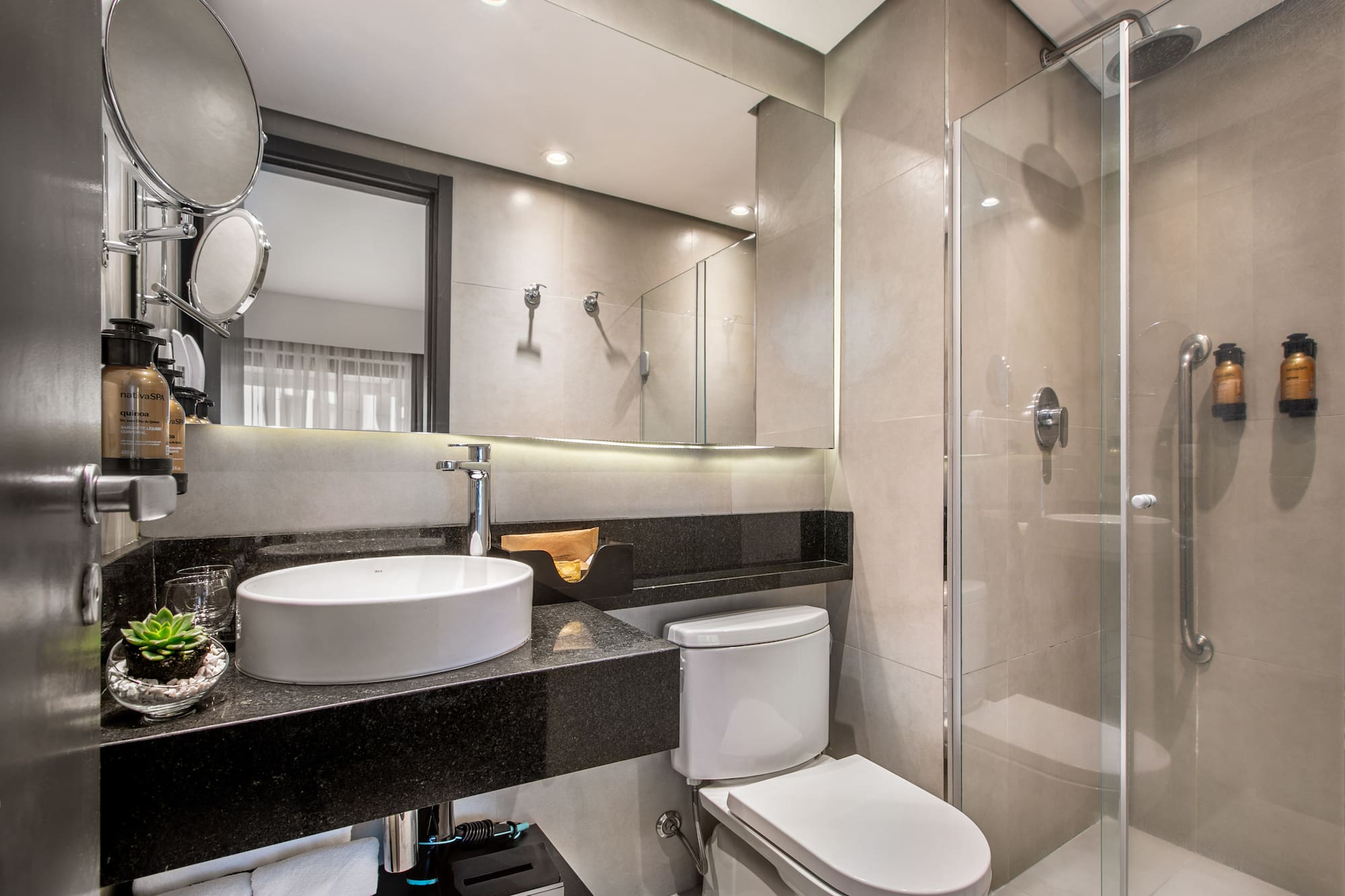 Modern hotel bathroom with white vessel sink, black granite vanity, toilet, and glass shower enclosure. - Deluxe Queen Room com Varanda - Meliá Ibirapuera, São Paulo