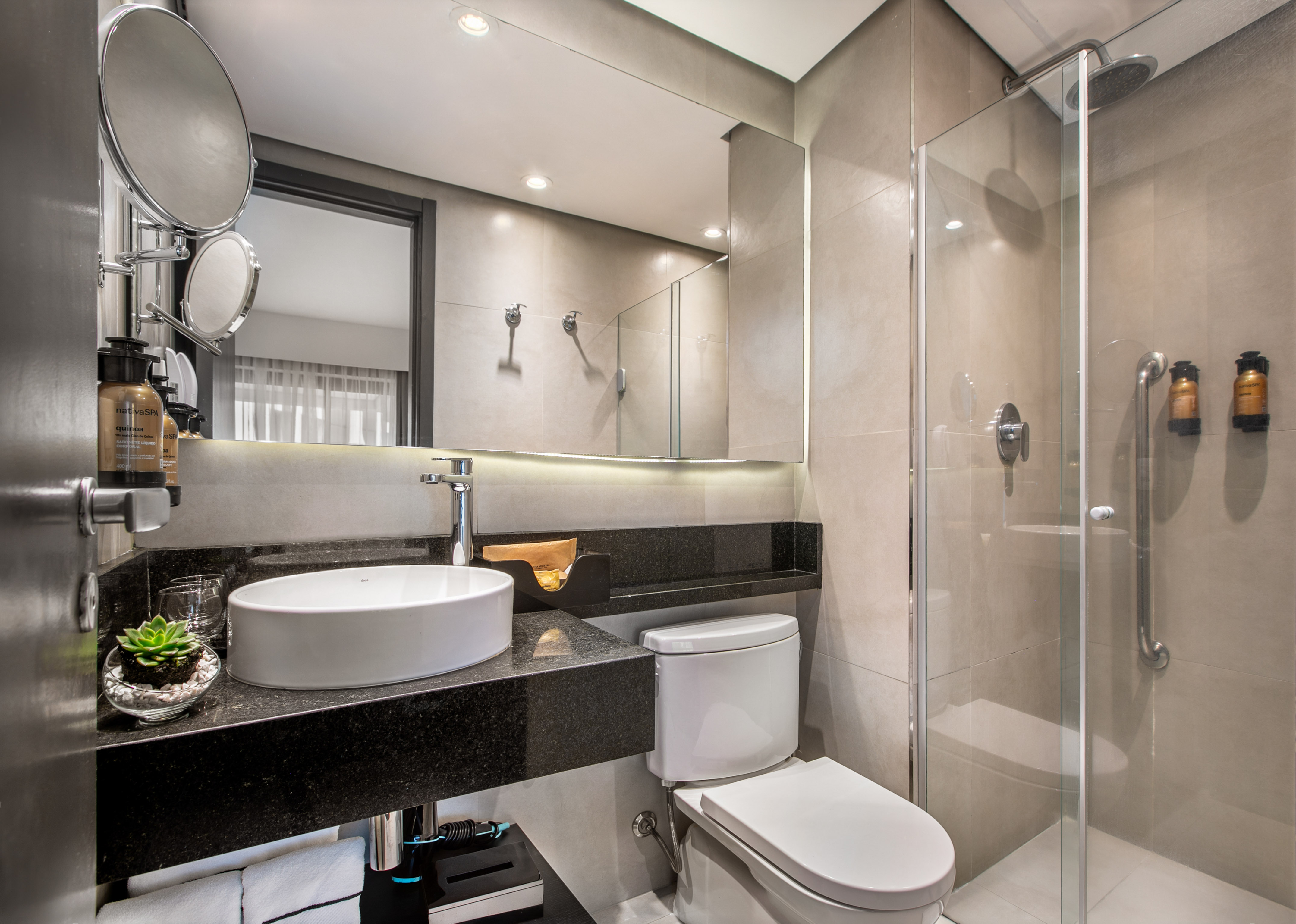 Modern hotel bathroom with white vessel sink, black granite vanity, toilet, and glass shower enclosure. - Deluxe Queen Room com Varanda - Meliá Ibirapuera, São Paulo
