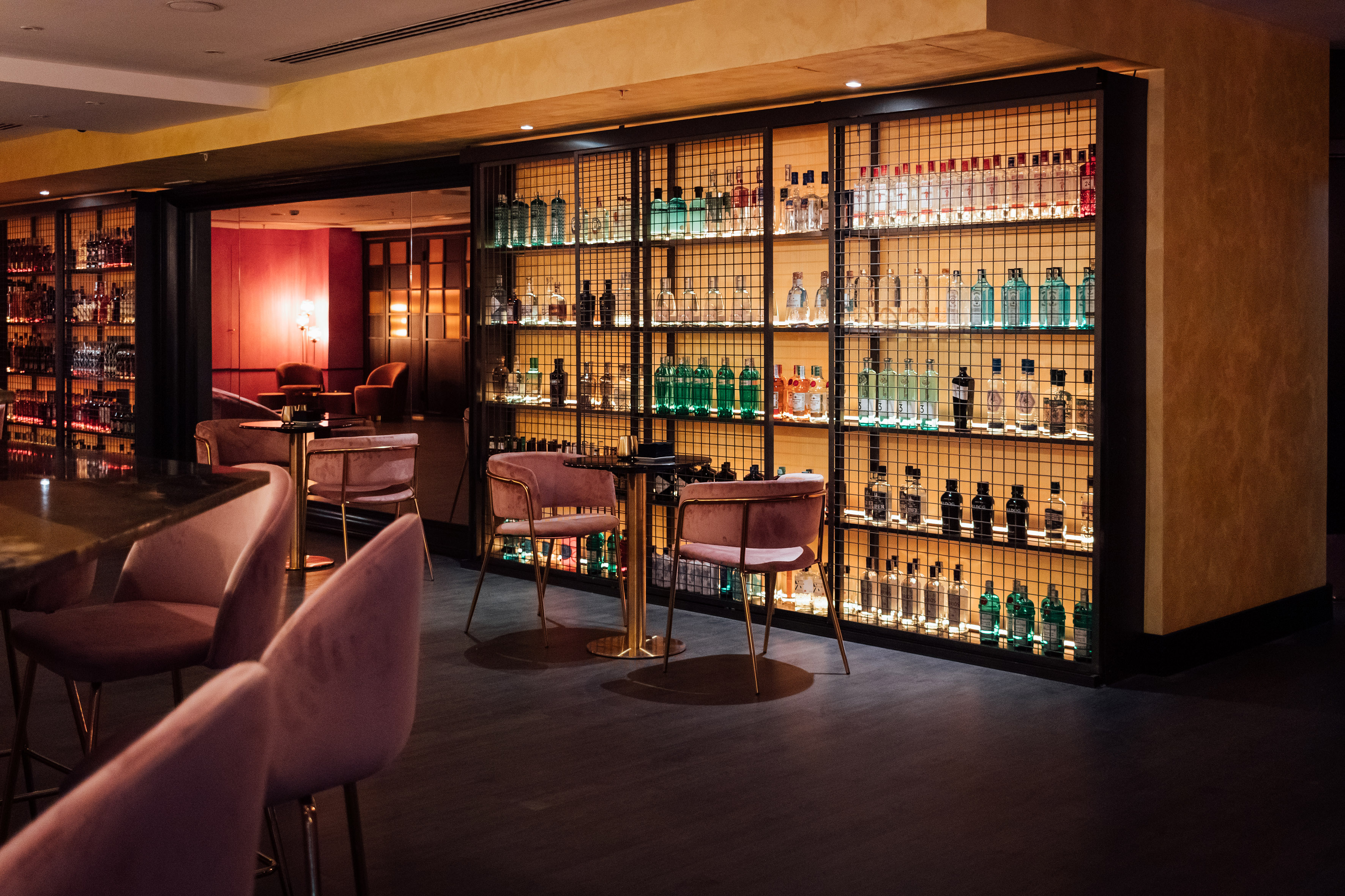 Modern bar with illuminated spirits shelves and pink velvet chairs.