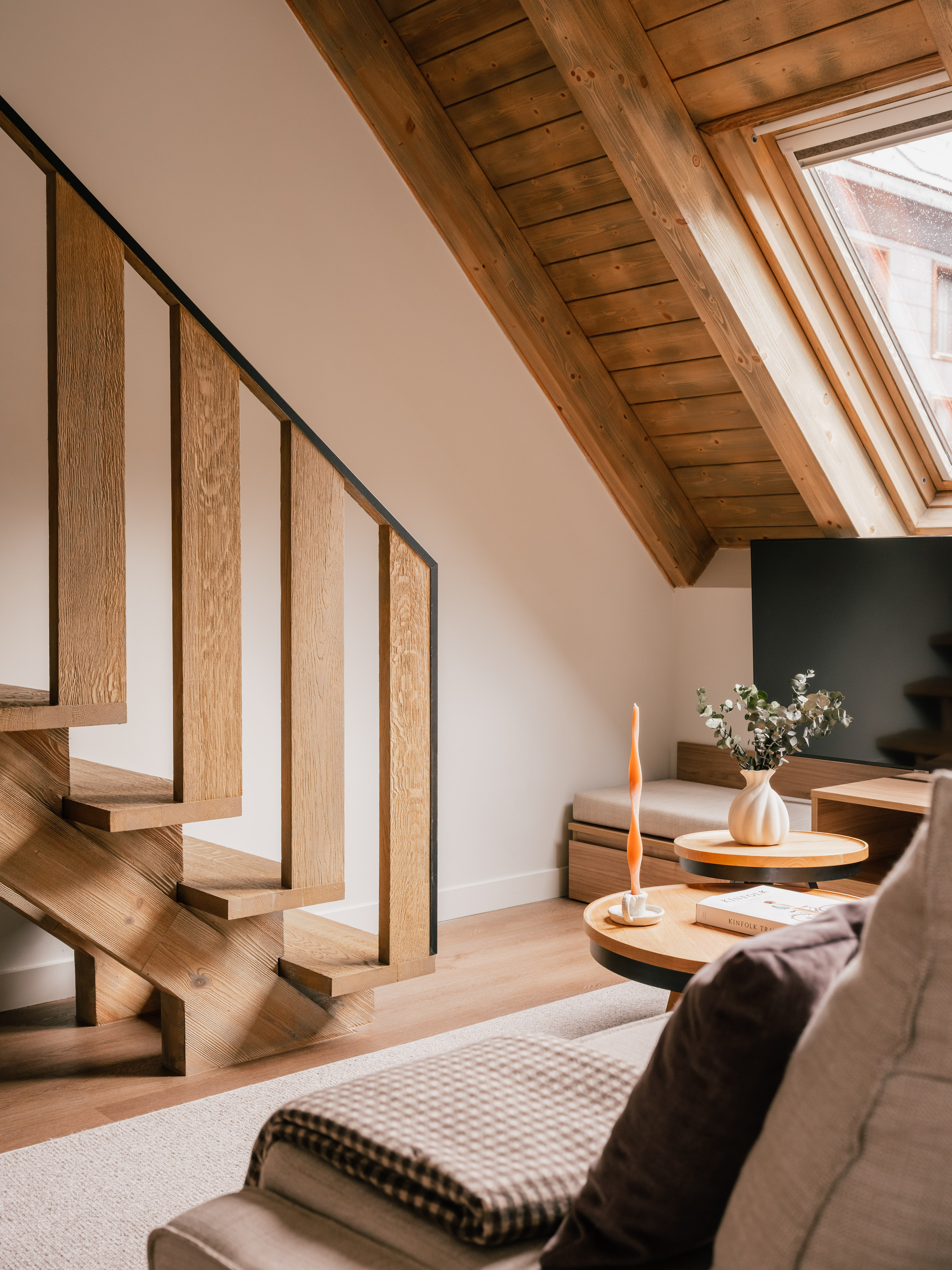 Modern living room with wooden staircase, slanted ceiling, and attic skylight.