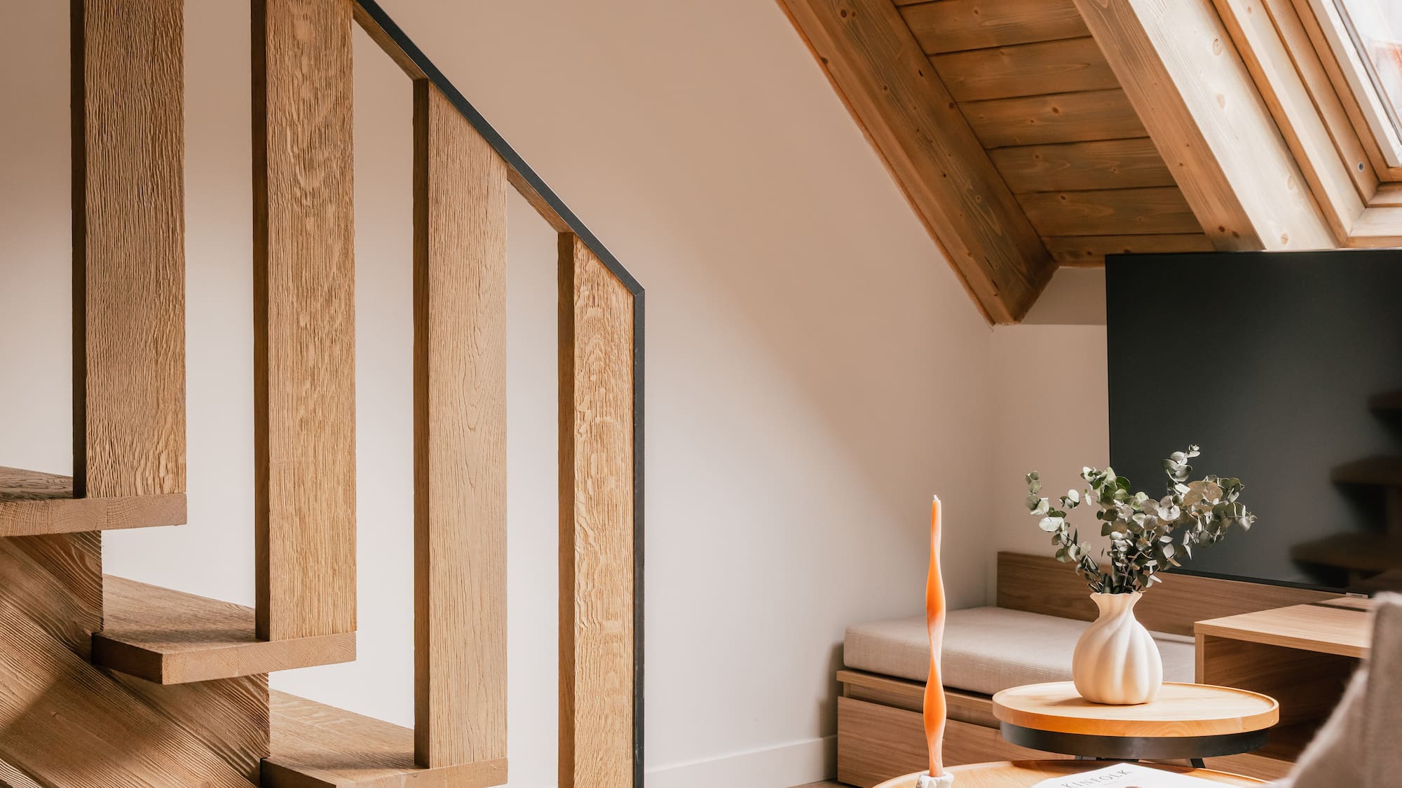 Modern living room with wooden staircase, slanted ceiling, and attic skylight.