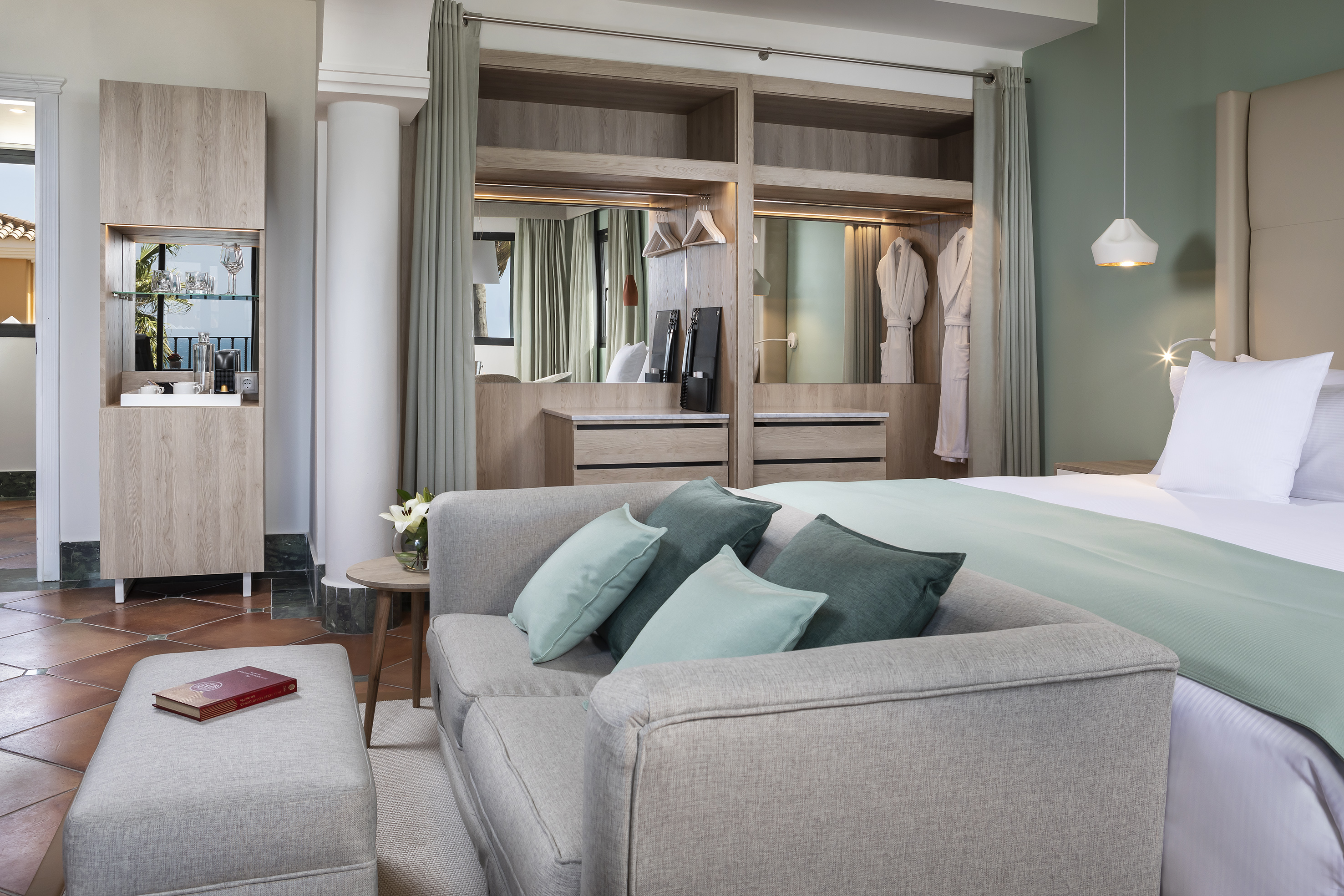 Stylish hotel suite: bed, sofa, built-in wardrobe, coffee station.