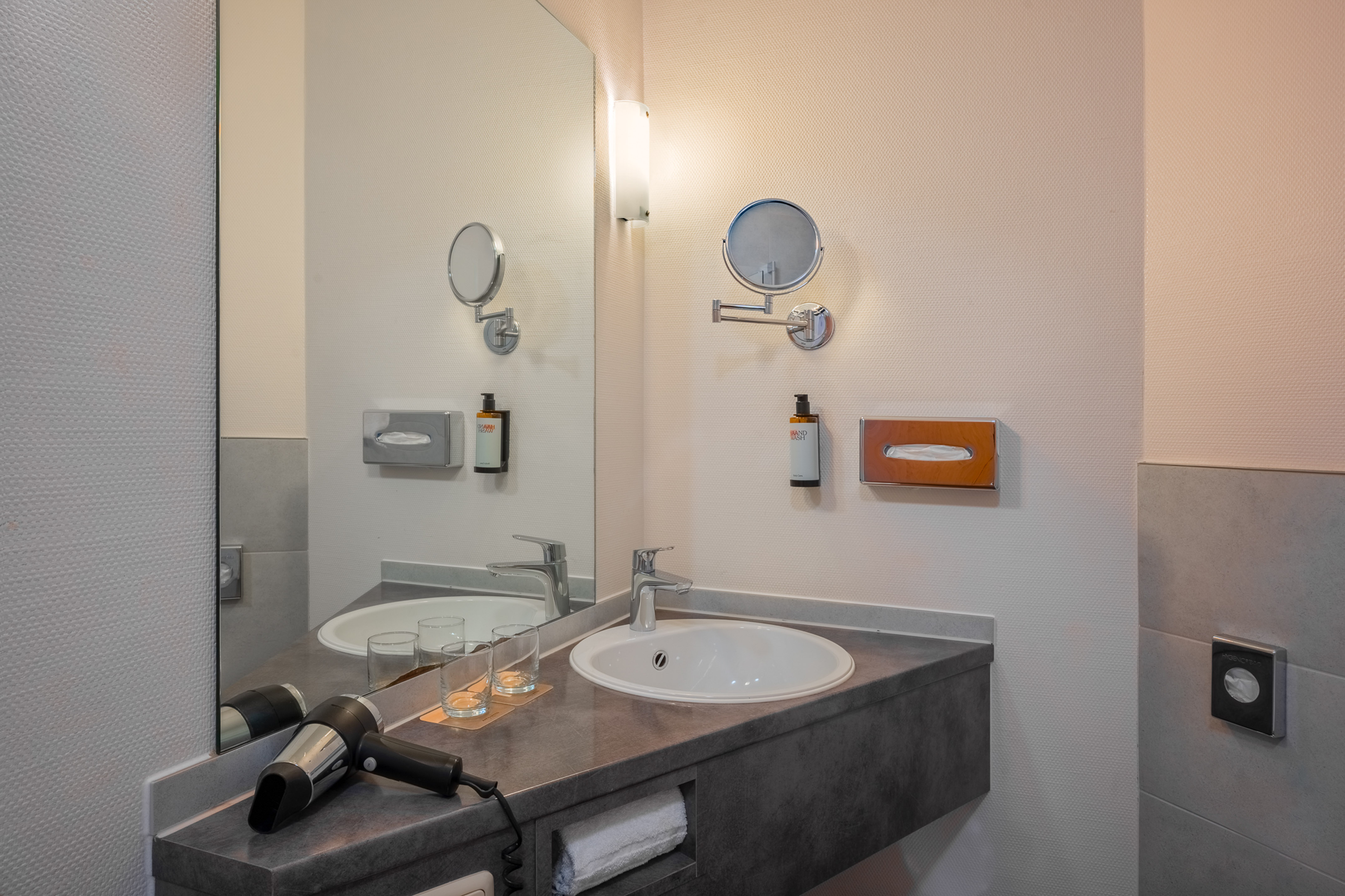 Sleek hotel bathroom with vanity, sink, magnifying mirror, and hairdryer.