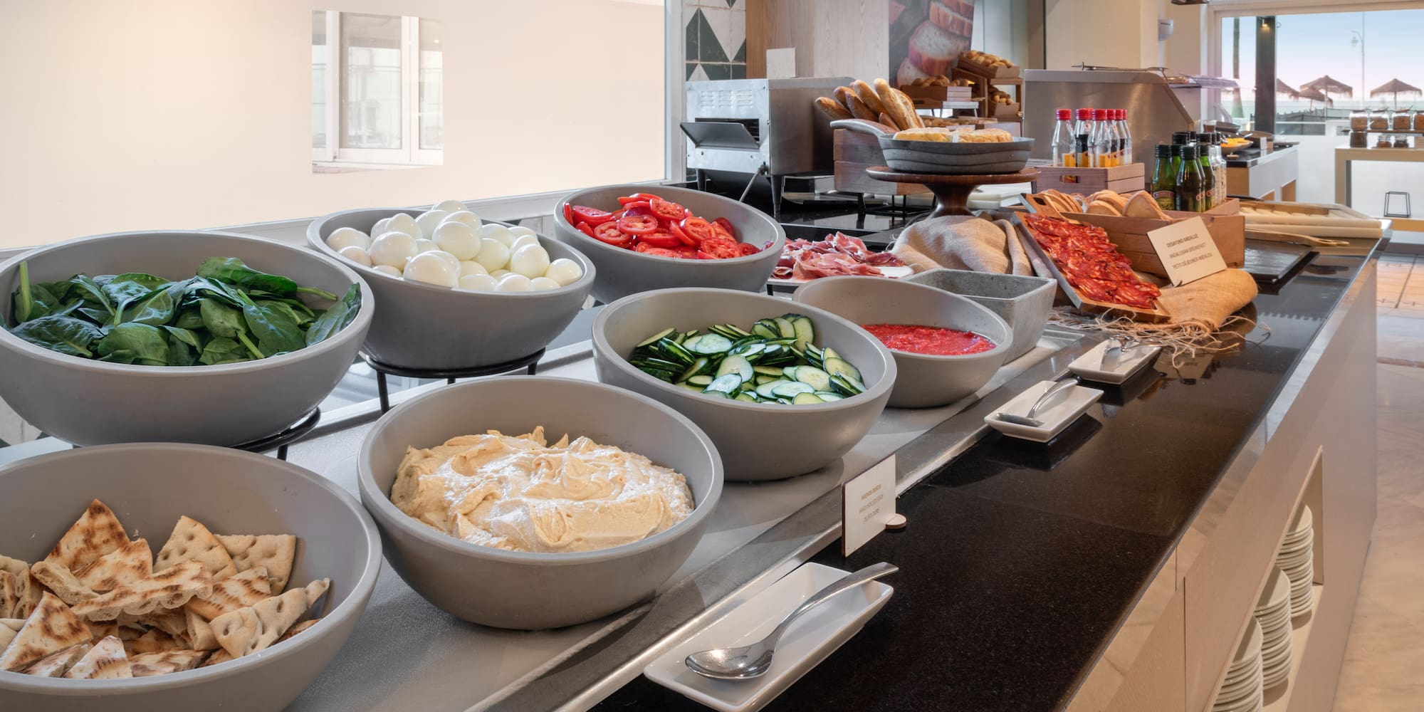 Hotel buffet with fresh spinach, boiled eggs, tomatoes, hummus, pita, and meats.