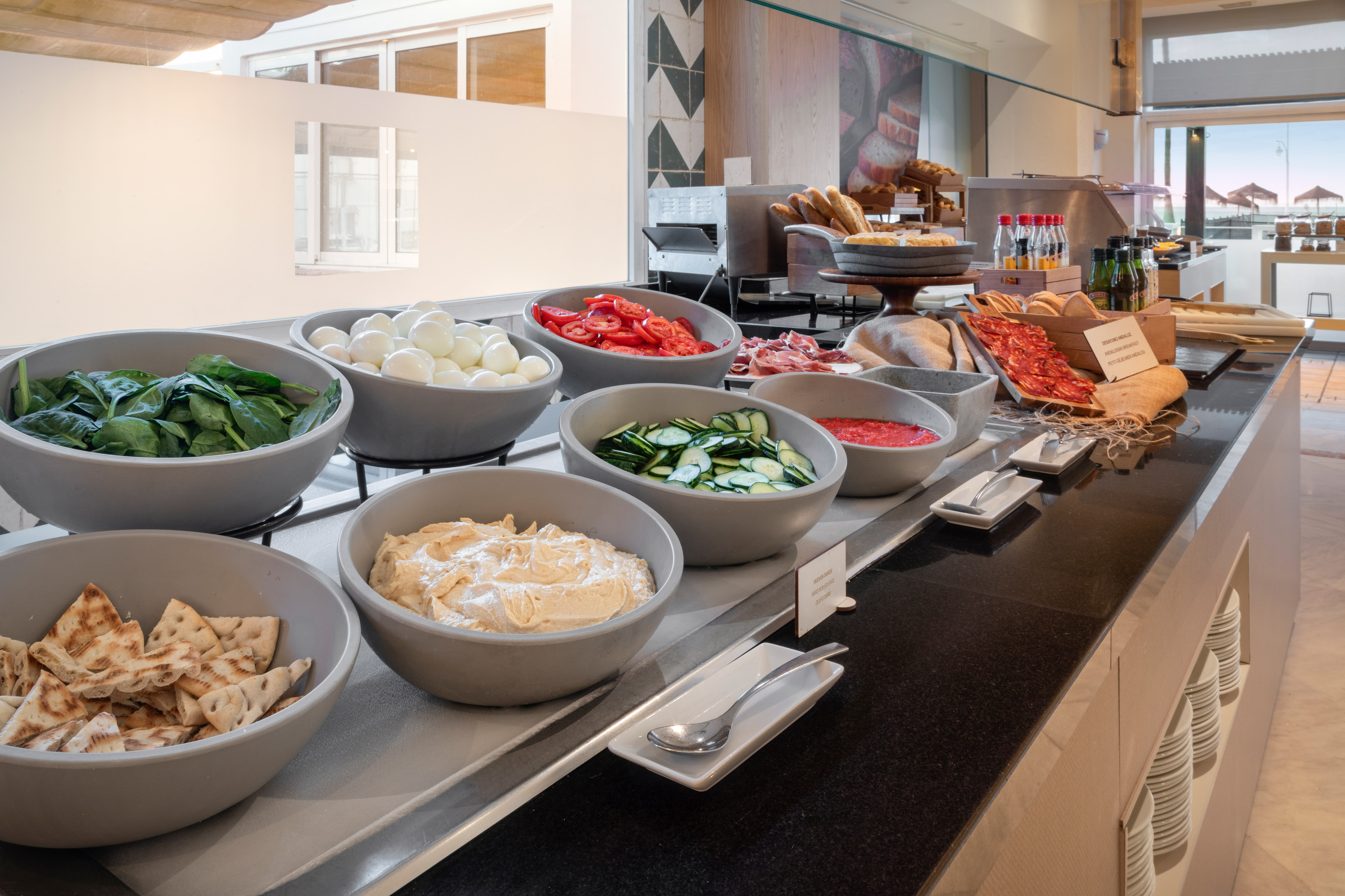 Hotel buffet with fresh spinach, boiled eggs, tomatoes, hummus, pita, and meats.
