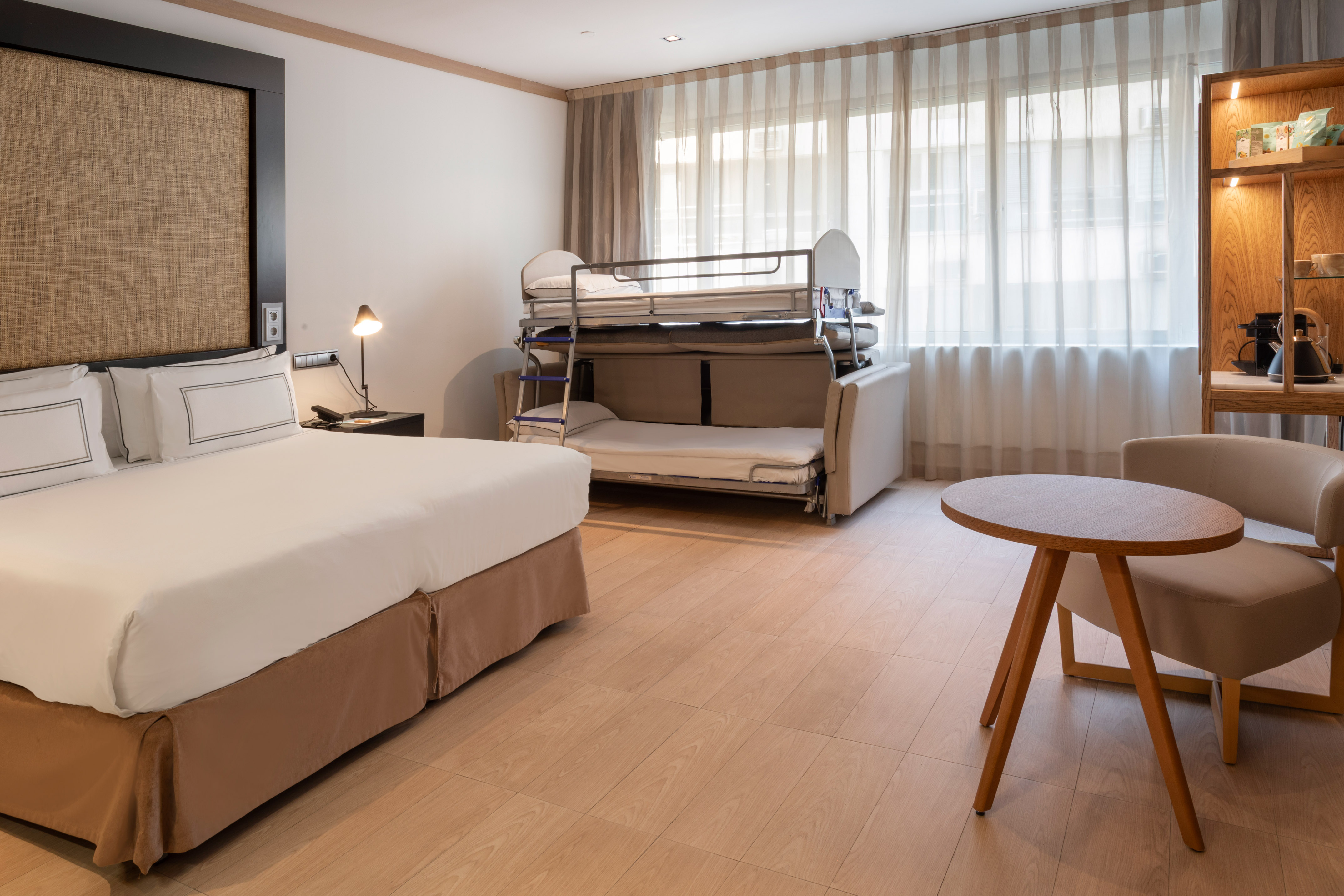 Habitación de hotel con camas individuales, sofá cama y pared de madera.