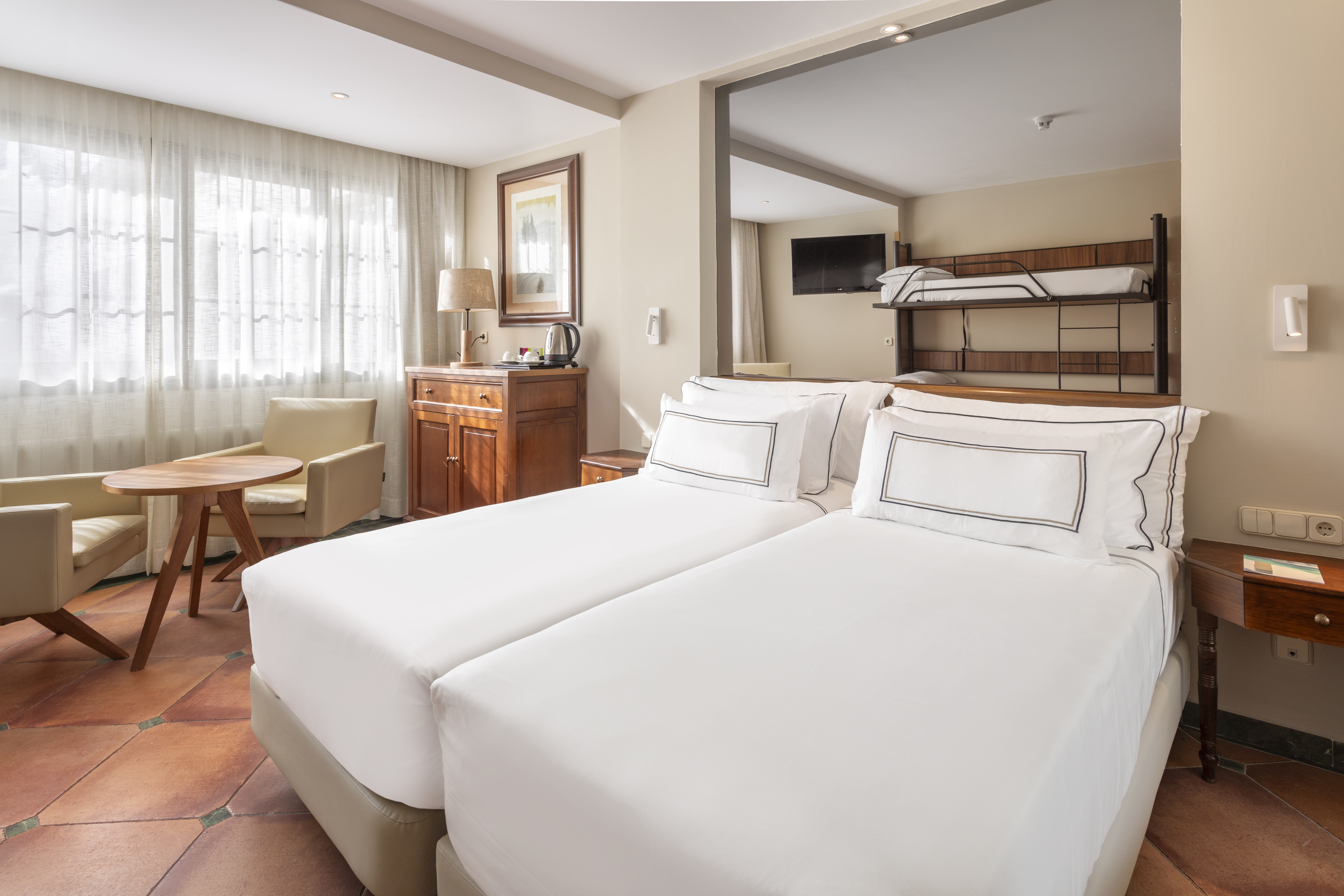 Hotel room with twin beds, bunk bed, sitting area, and terracotta floor.