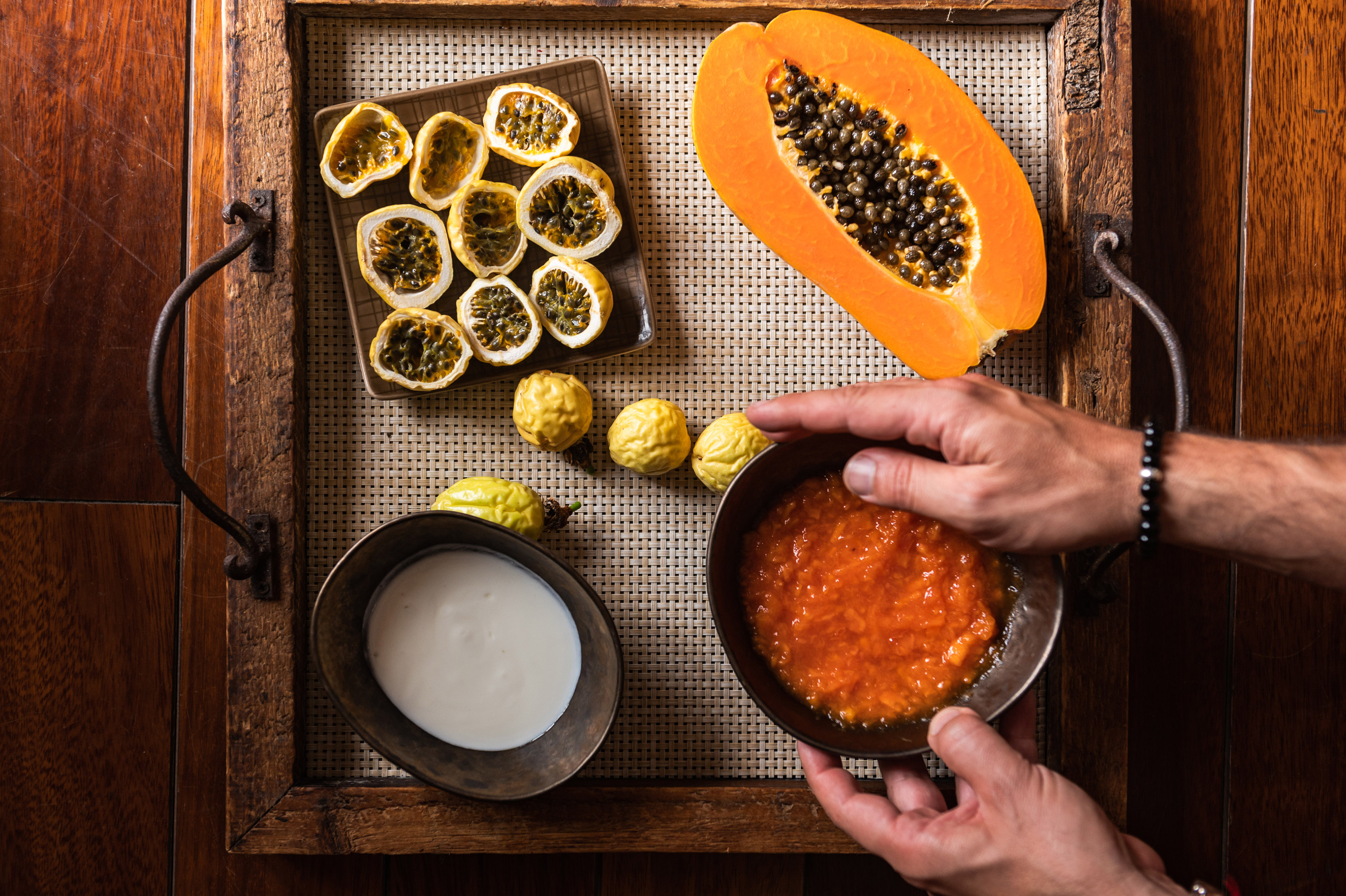 Hands holding papaya pulp bowl; fresh papaya, passion fruits on rustic tray.