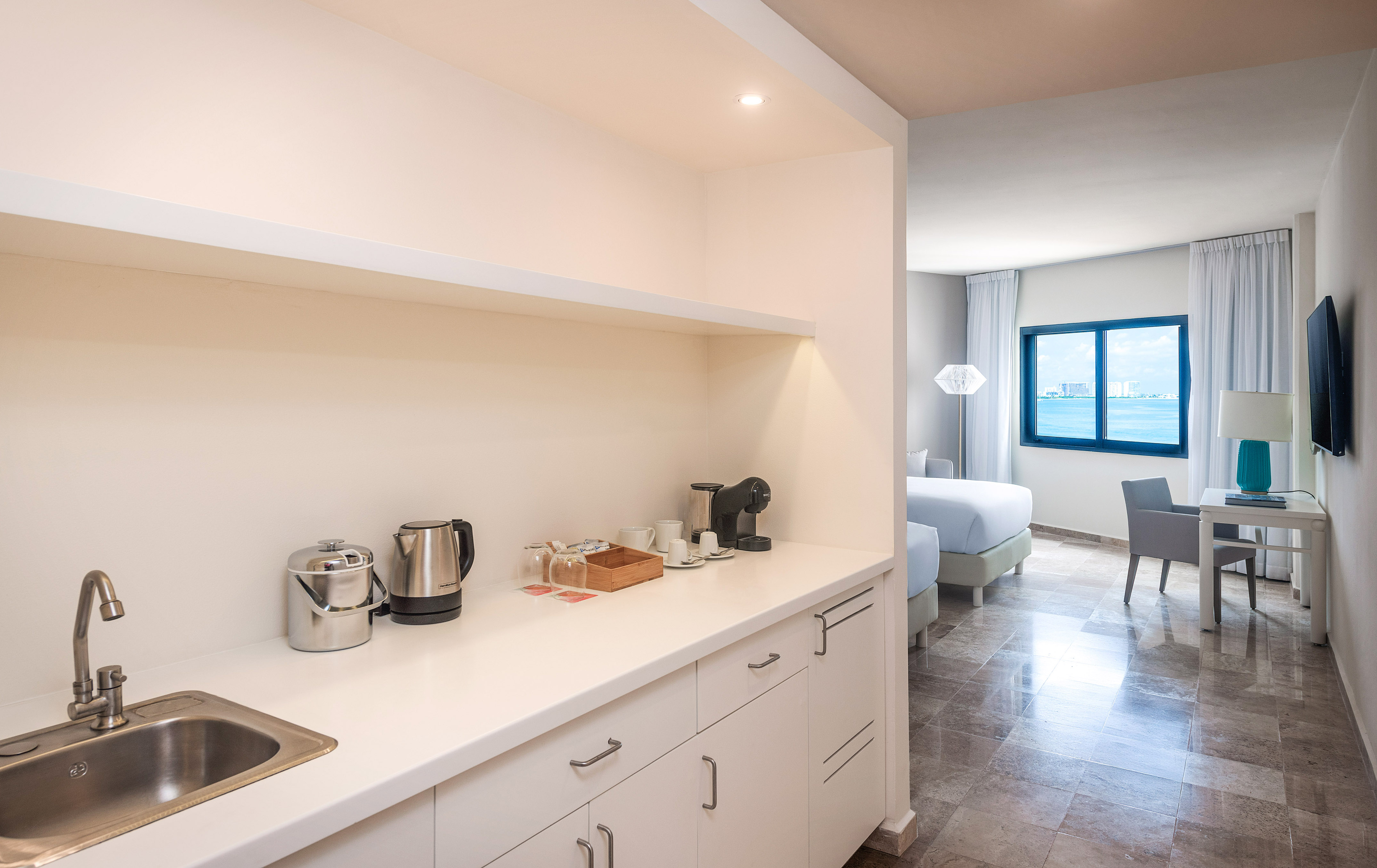 Hotel suite kitchenette with coffee maker, sink, and ocean view bedroom.