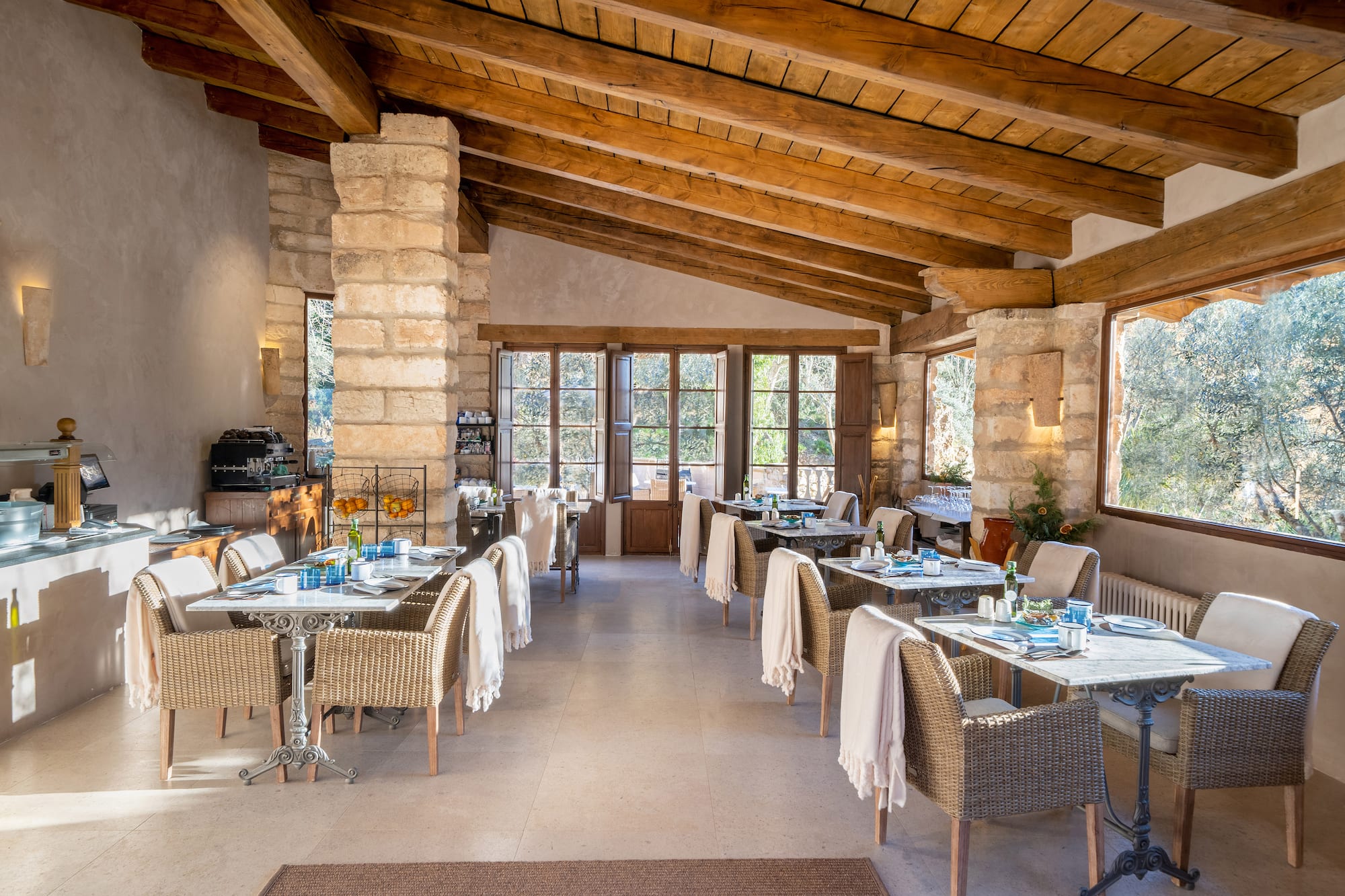 Rustic restaurant with stone walls, wooden beams, wicker chairs, and garden views.