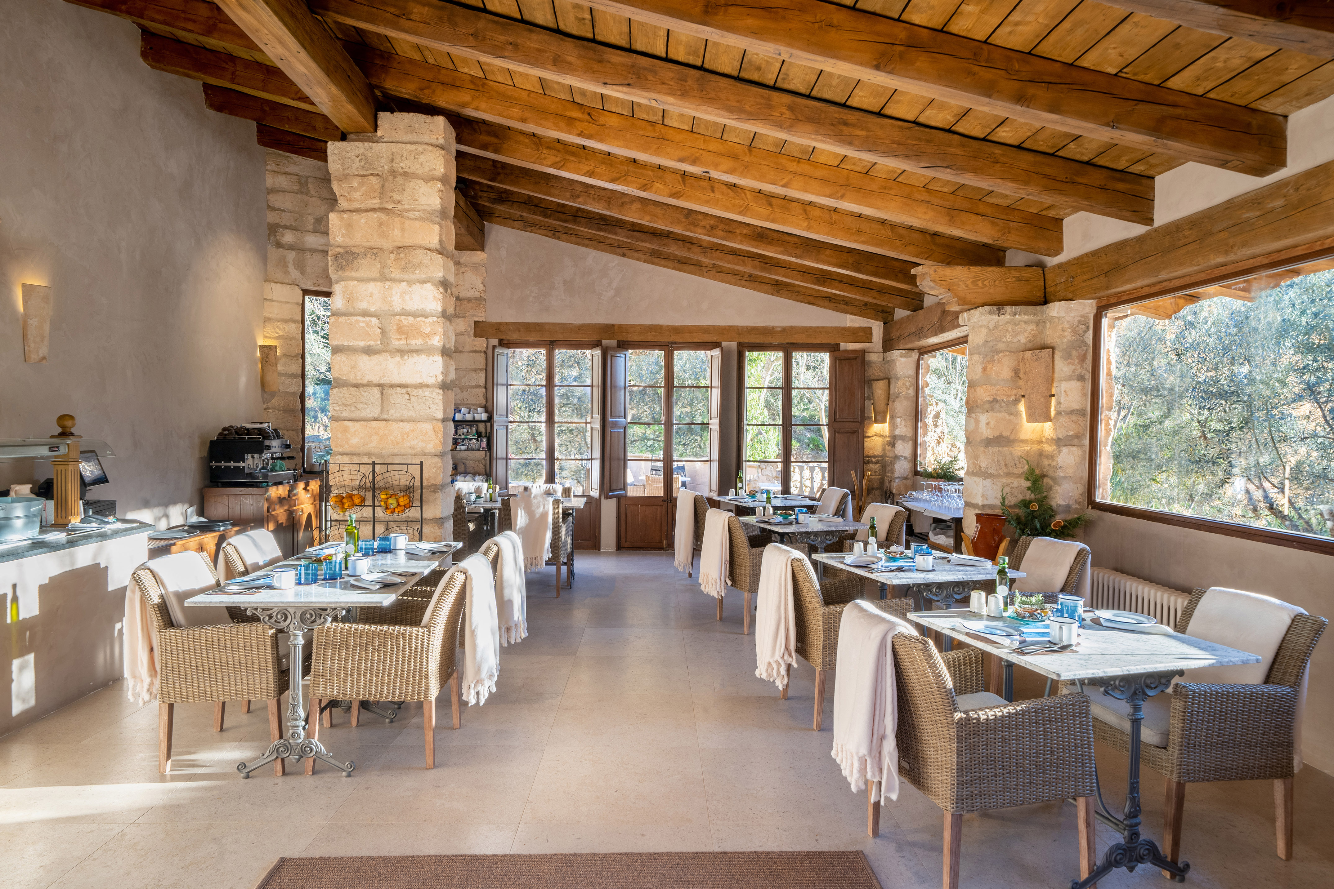 Rustic restaurant with stone walls, wooden beams, wicker chairs, and garden views.