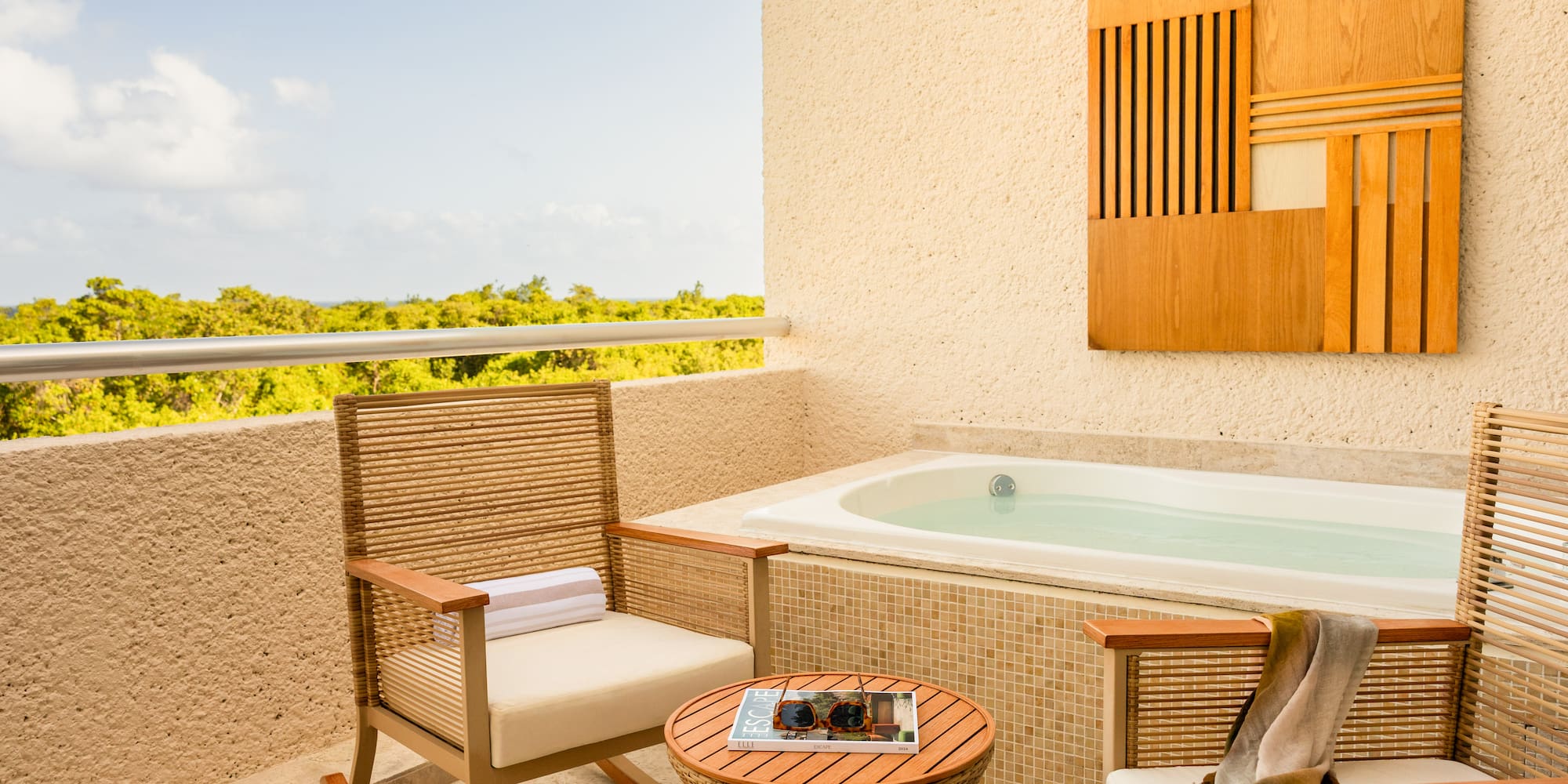 Hotel balcony with private hot tub, lounge chairs, and lush tropical view.