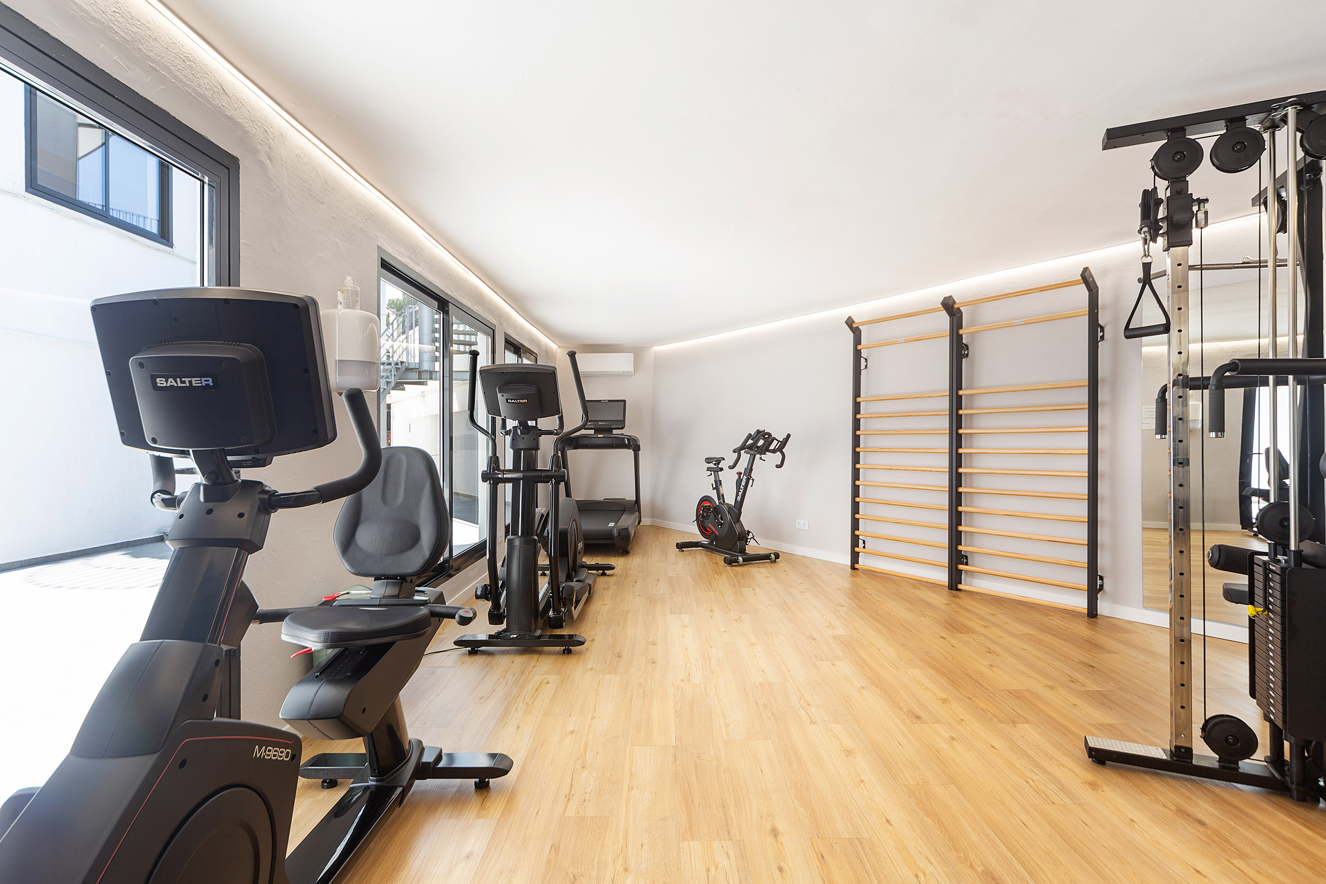 Bright modern gym with fitness equipment, treadmill, bikes, and stall bars.